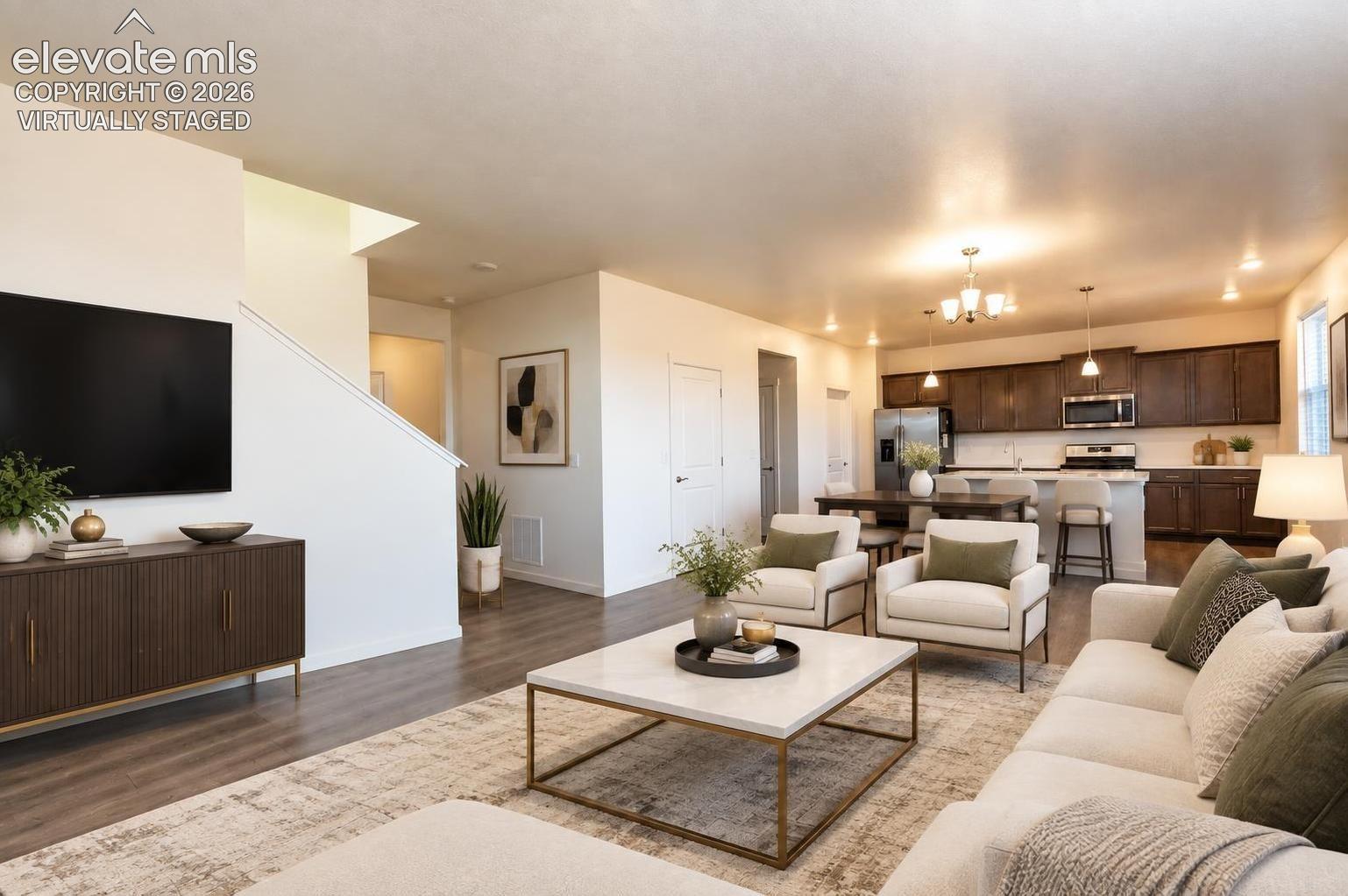Open-plan living room with white sofas and coffee table beside a kitchen with dark cabinets and stainless steel appliances.