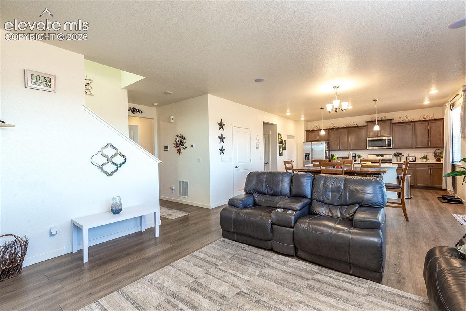Open-plan living room with a dark leather reclining sofa, dining area, and brown-cabinet kitchen.