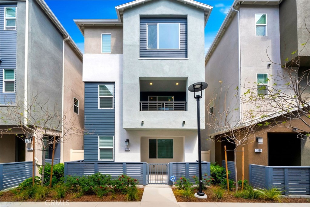 Three-story gray townhouse with a blue-gray balcony, fenced garden, and centered front walkway.
