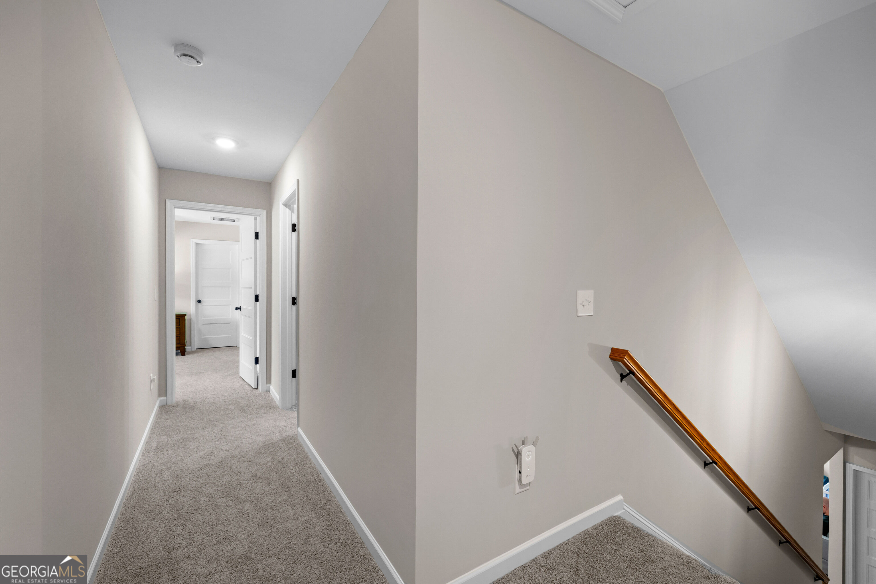 Carpeted upstairs hallway beside a stairwell with a wooden handrail.