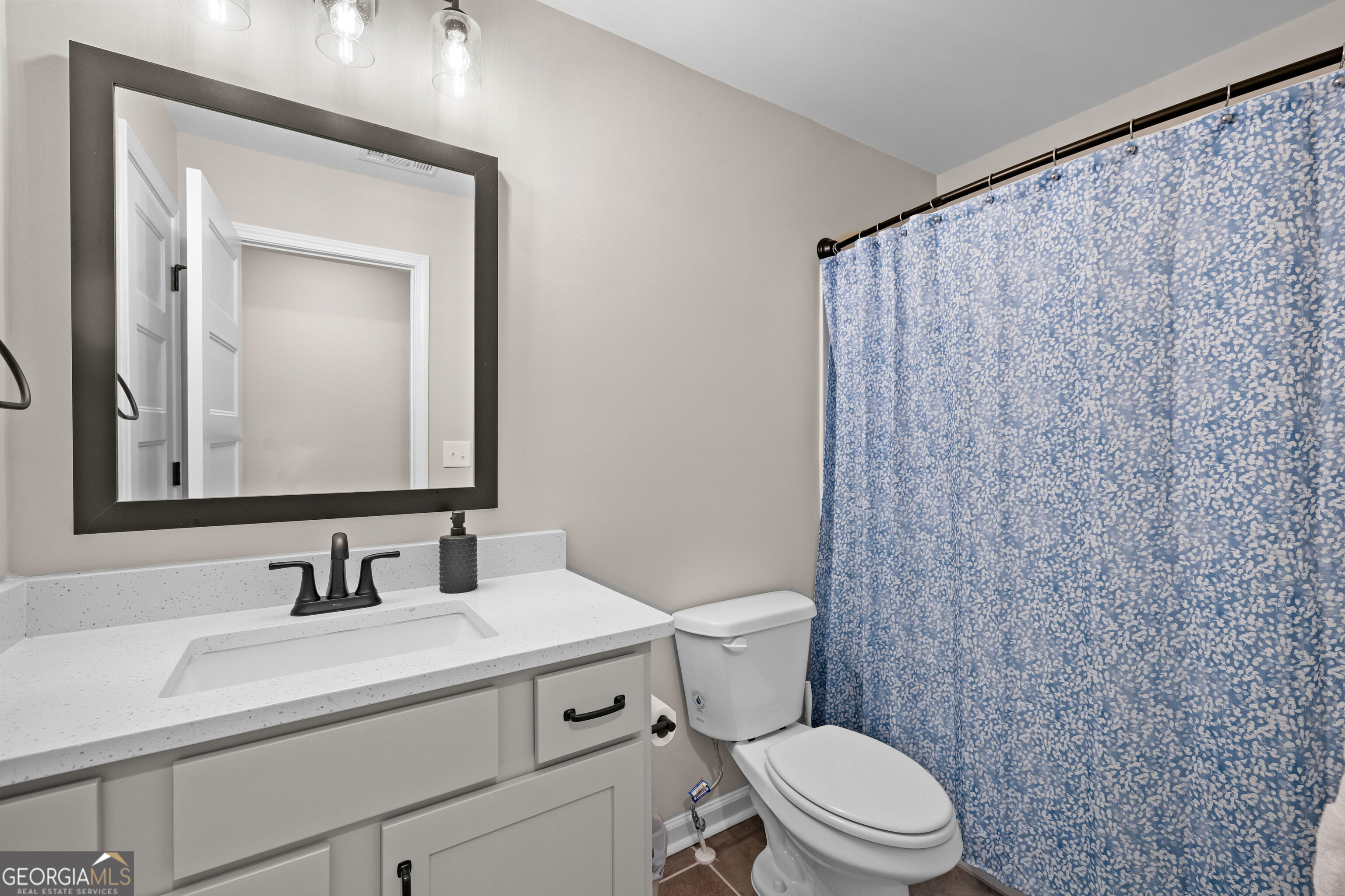 Bathroom with a white vanity, dark-framed mirror, and blue patterned shower curtain.