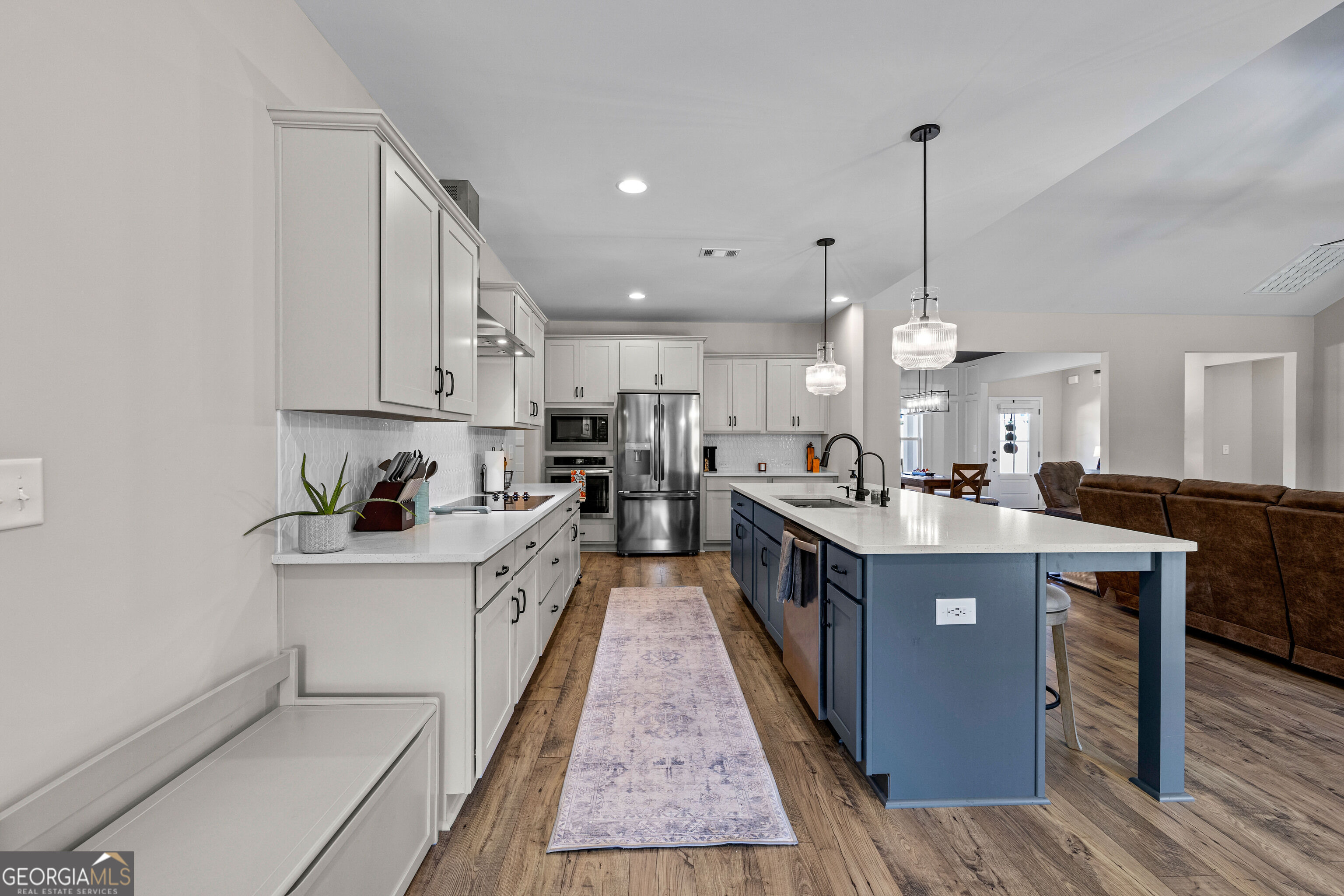 Open kitchen with white cabinets, stainless steel appliances, and a large blue island beside the living area.