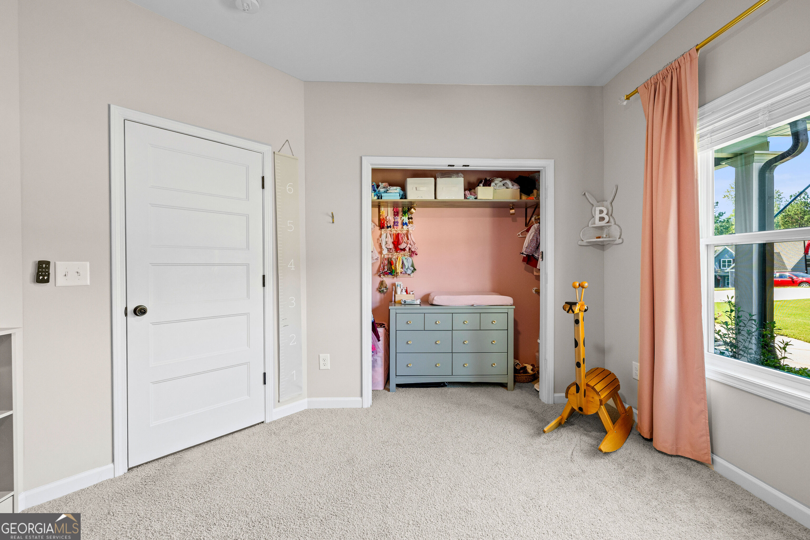 Child’s bedroom with an open pink closet, dresser, and wooden giraffe toy.
