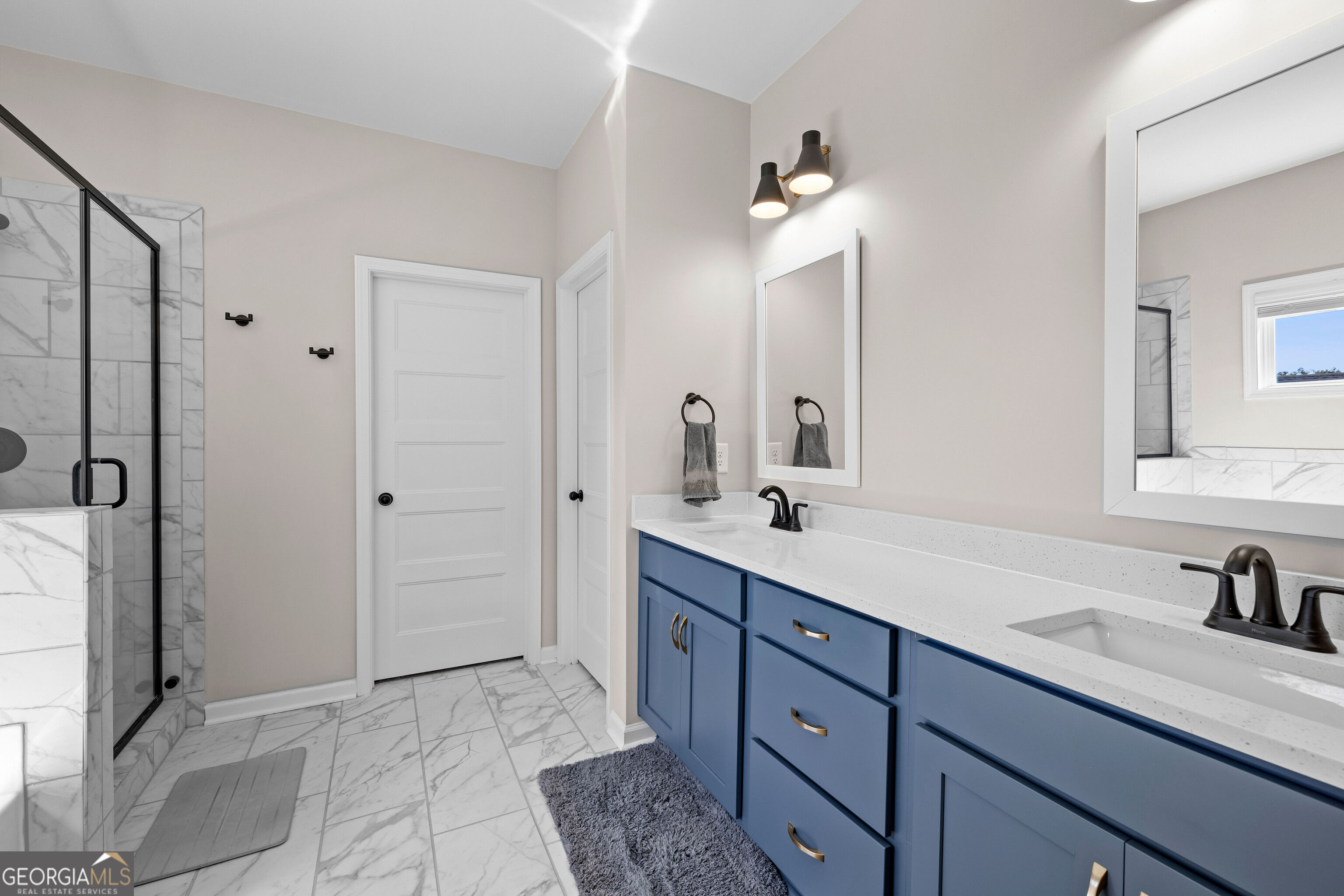 Bathroom with blue double vanity, brass pulls, and a marble-look glass-enclosed shower.