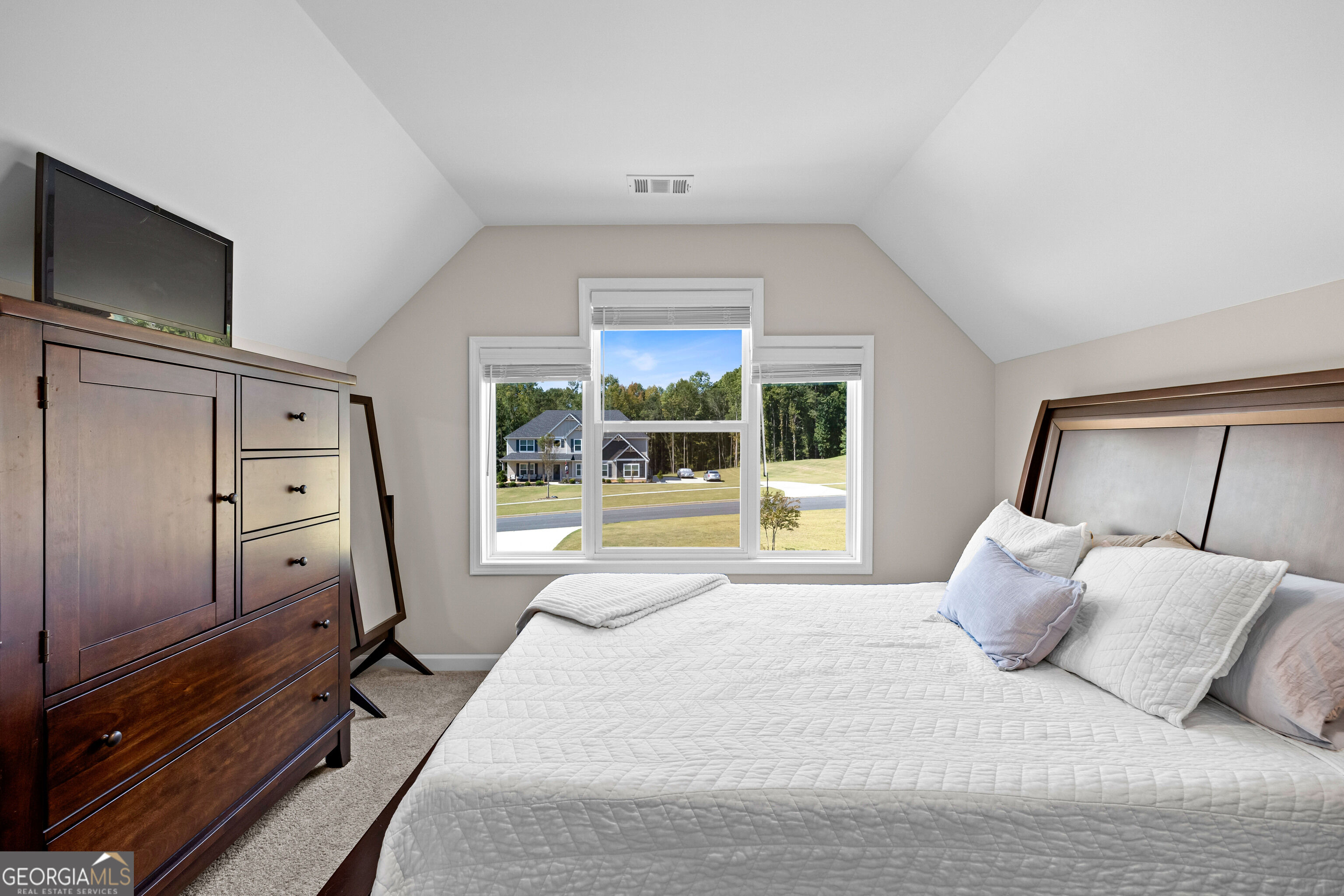 Bedroom with a large white bed, dark wood dresser, and three windows overlooking a neighboring home.