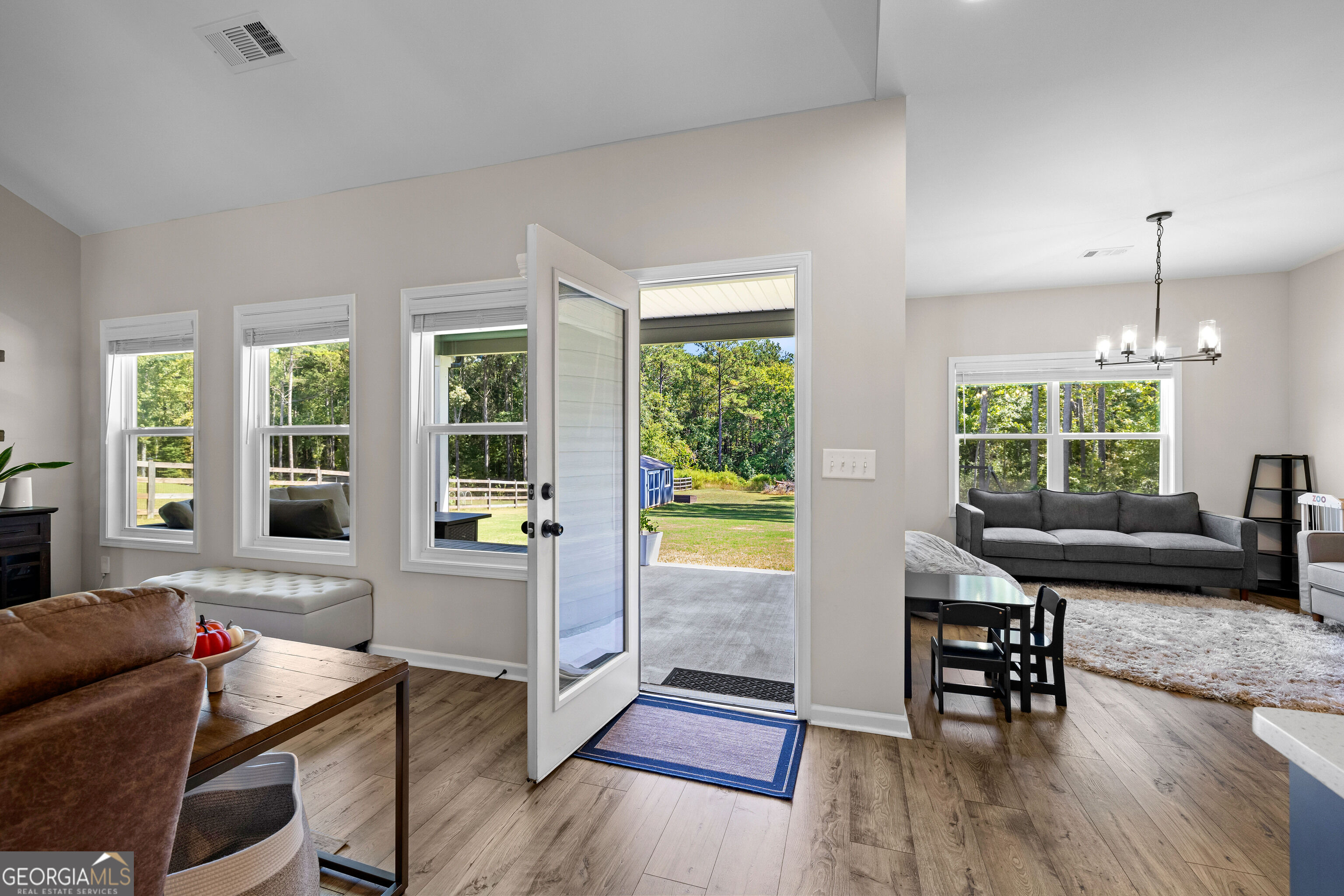 Furnished living room with an open door to a covered patio and tree-lined yard.