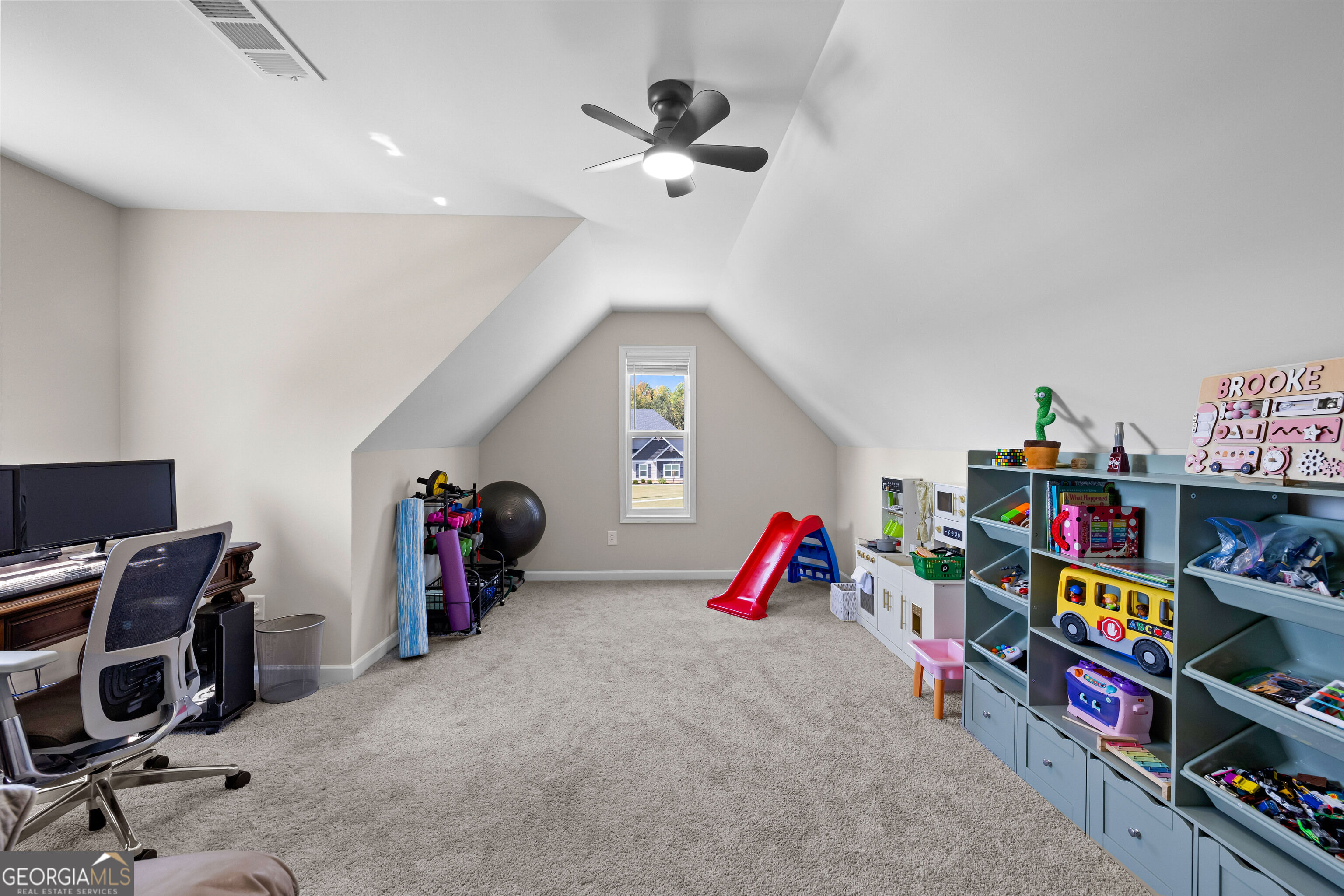 Upstairs playroom with vaulted ceiling, toy shelves, red slide, and a desk by the window.