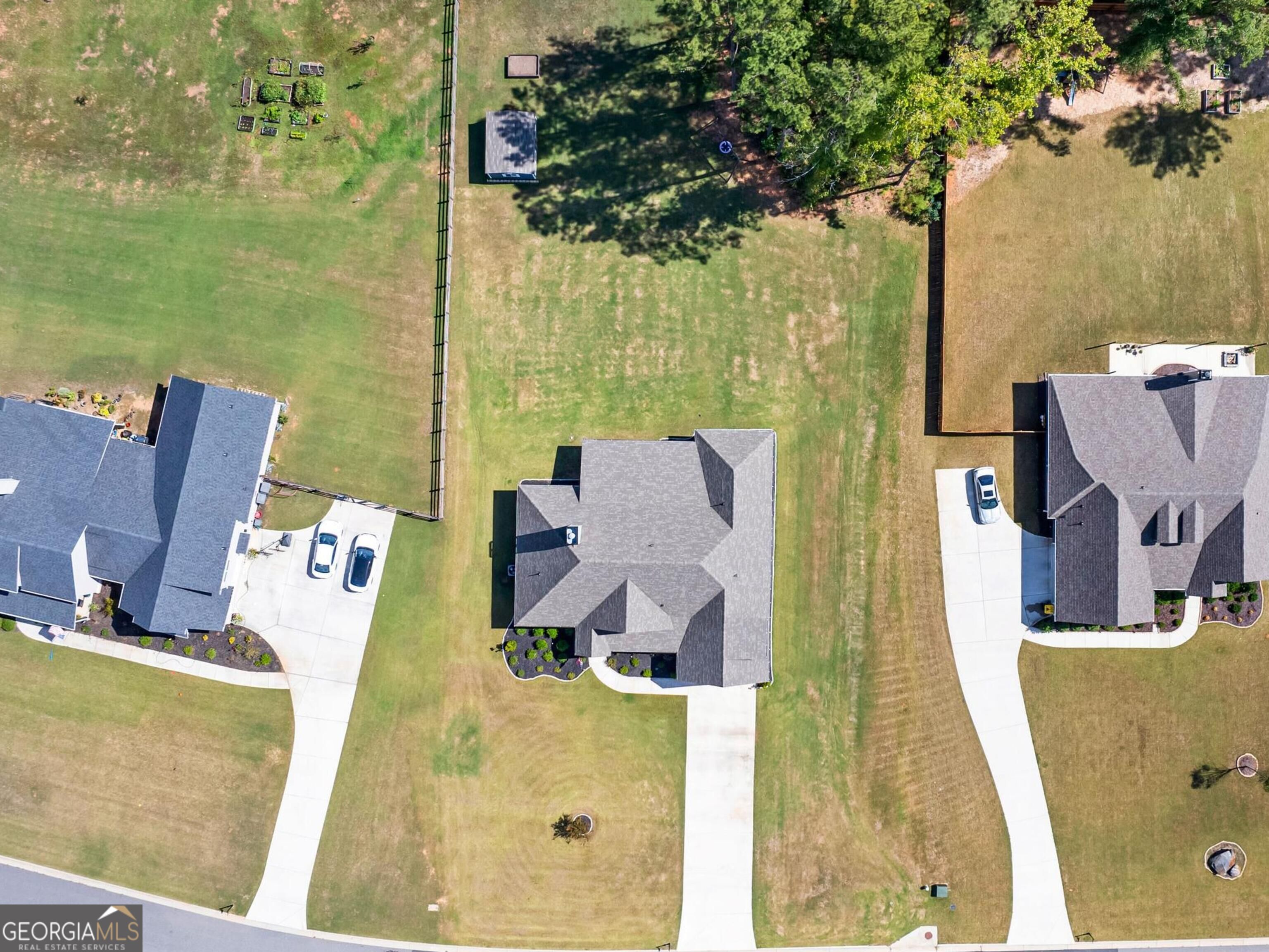 Aerial view of a gray-roofed home with a broad lawn and driveway between neighboring houses.
