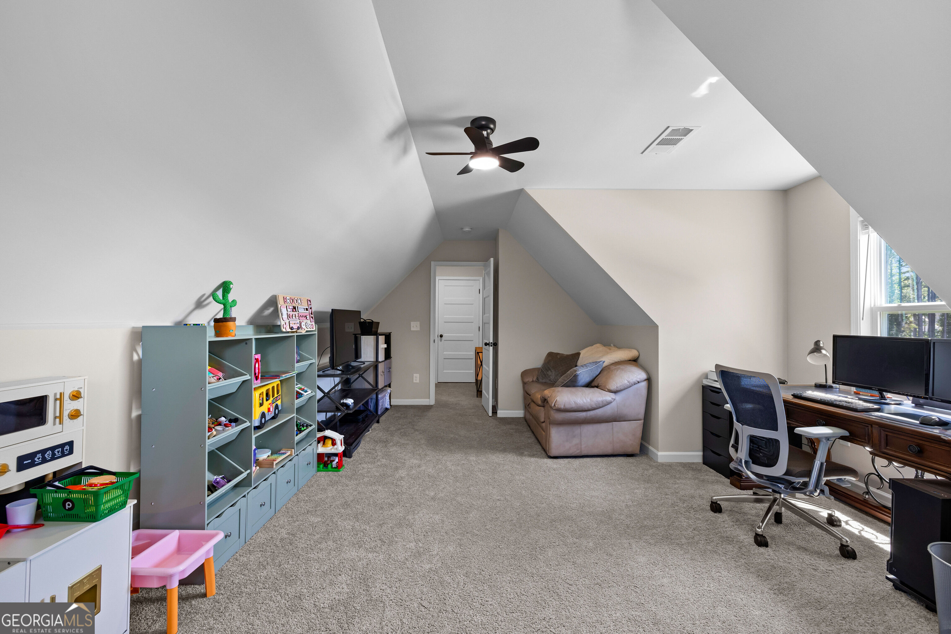 Furnished bonus room with a sloped ceiling, toy storage, sofa, and computer workstation.