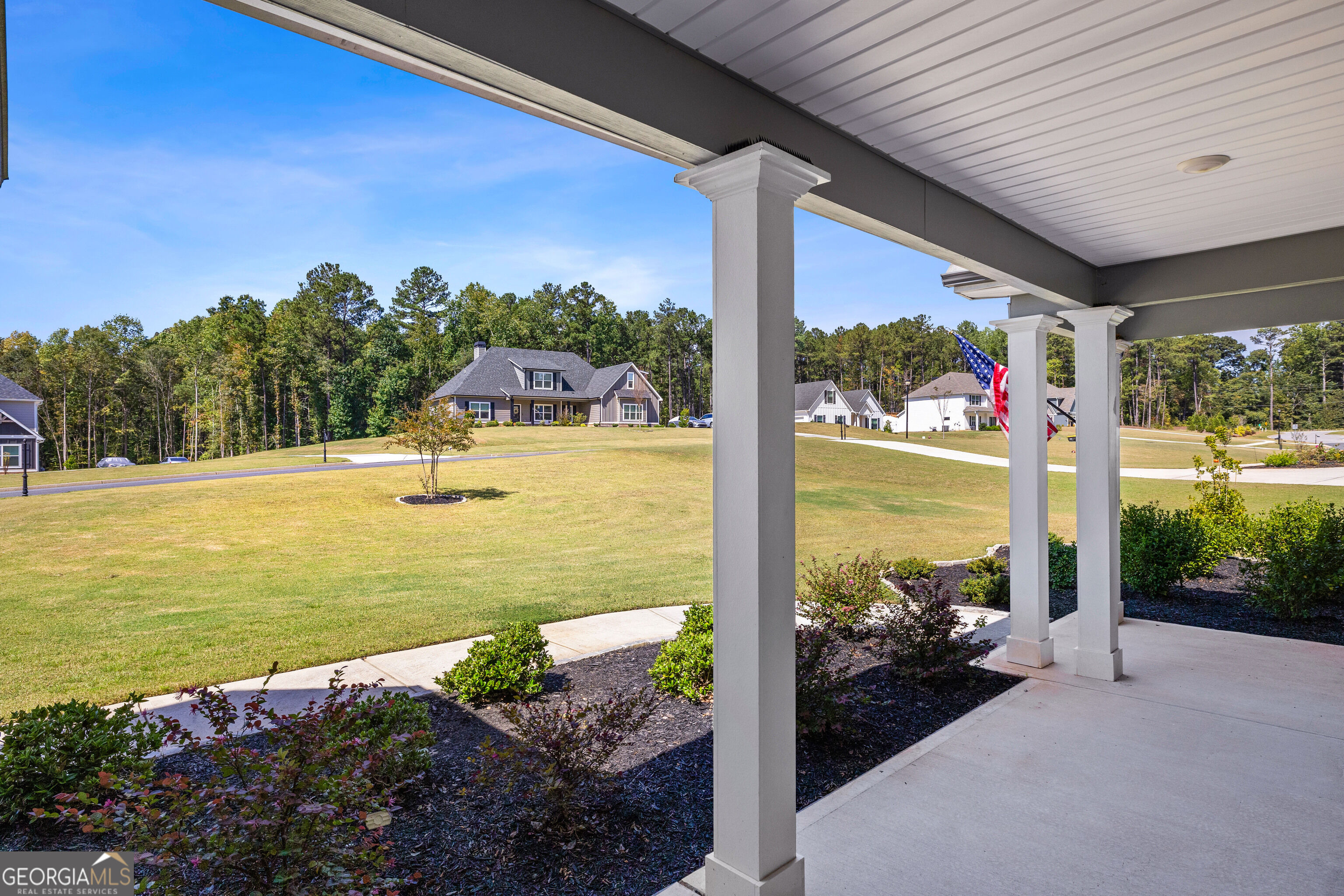 Covered porch with white columns overlooking a landscaped lawn and neighboring homes.