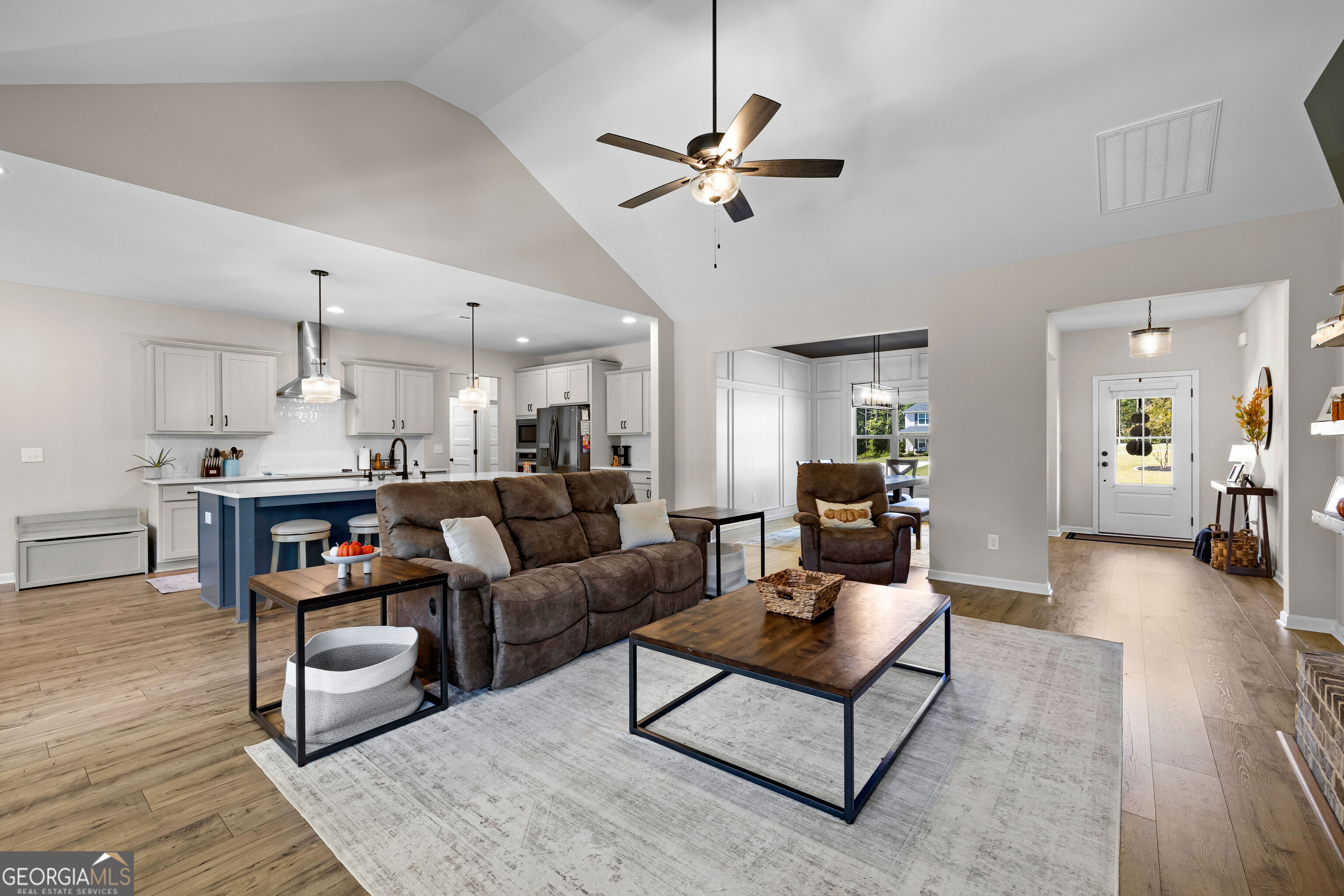 Open living room and kitchen with a blue island, brown reclining sofa, and vaulted ceiling.