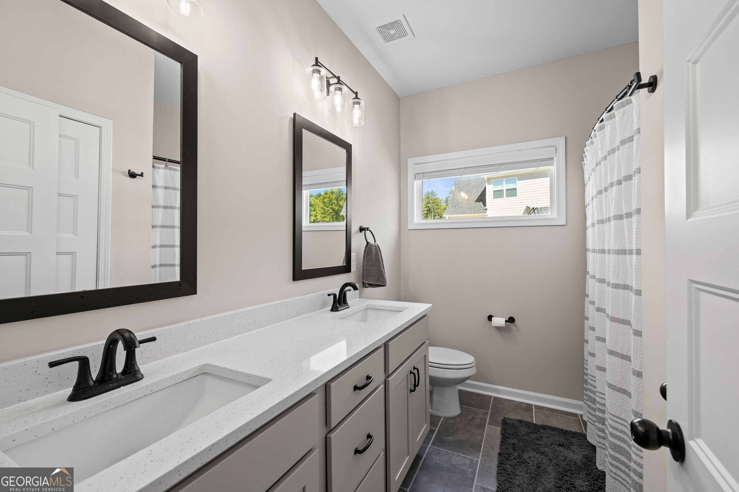 Bathroom with double vanity, black-framed mirrors, and gray striped shower curtain.