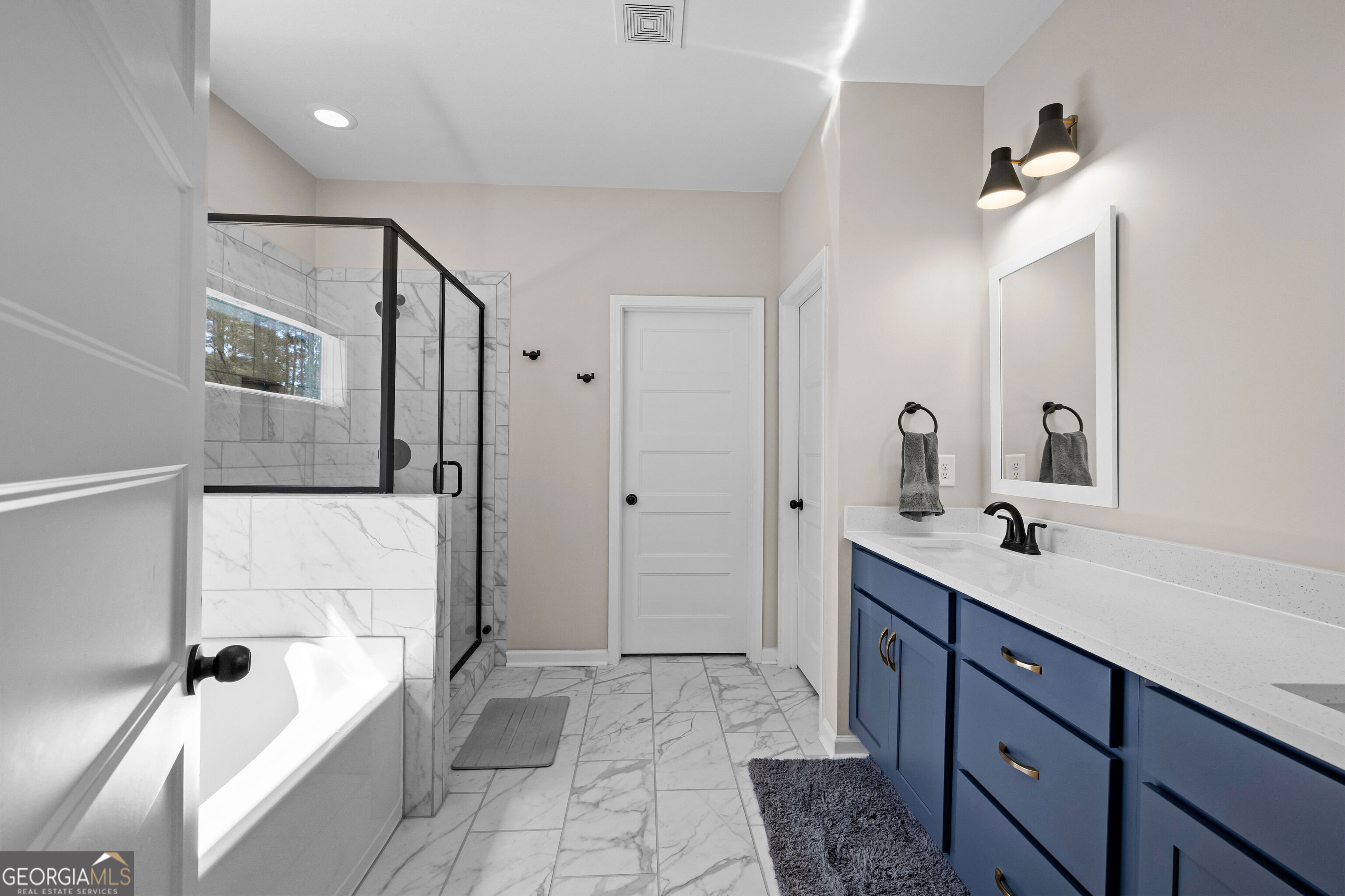 Bathroom with a black-framed glass shower, marble-look tile, and deep blue vanity.