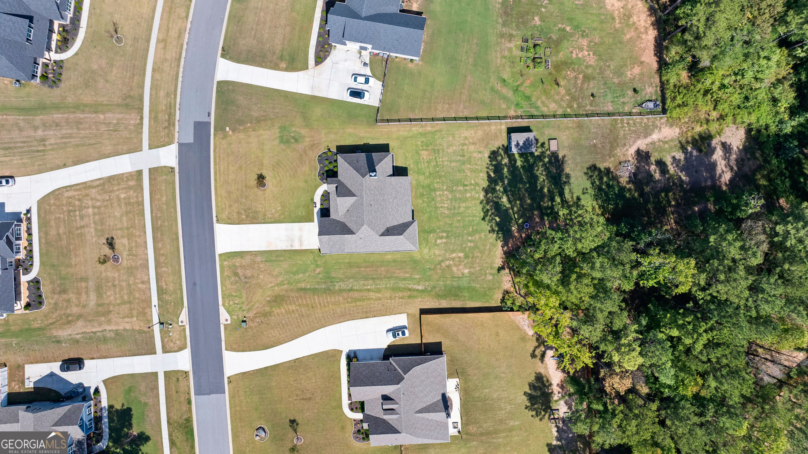 Aerial view of a house with a broad lawn beside dense woods and a residential street.