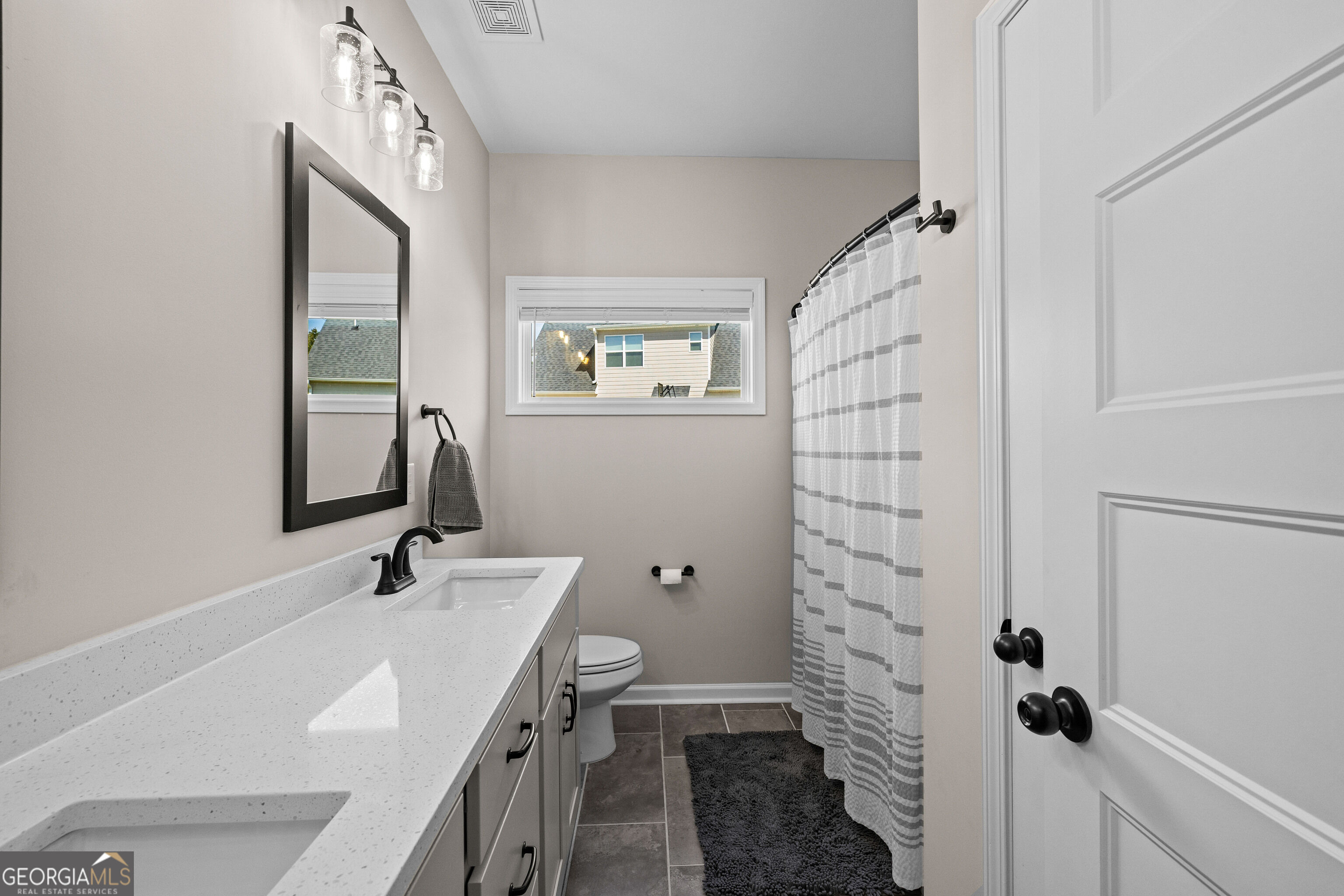 Bathroom with a long double-sink vanity, black fixtures, and a striped shower curtain.