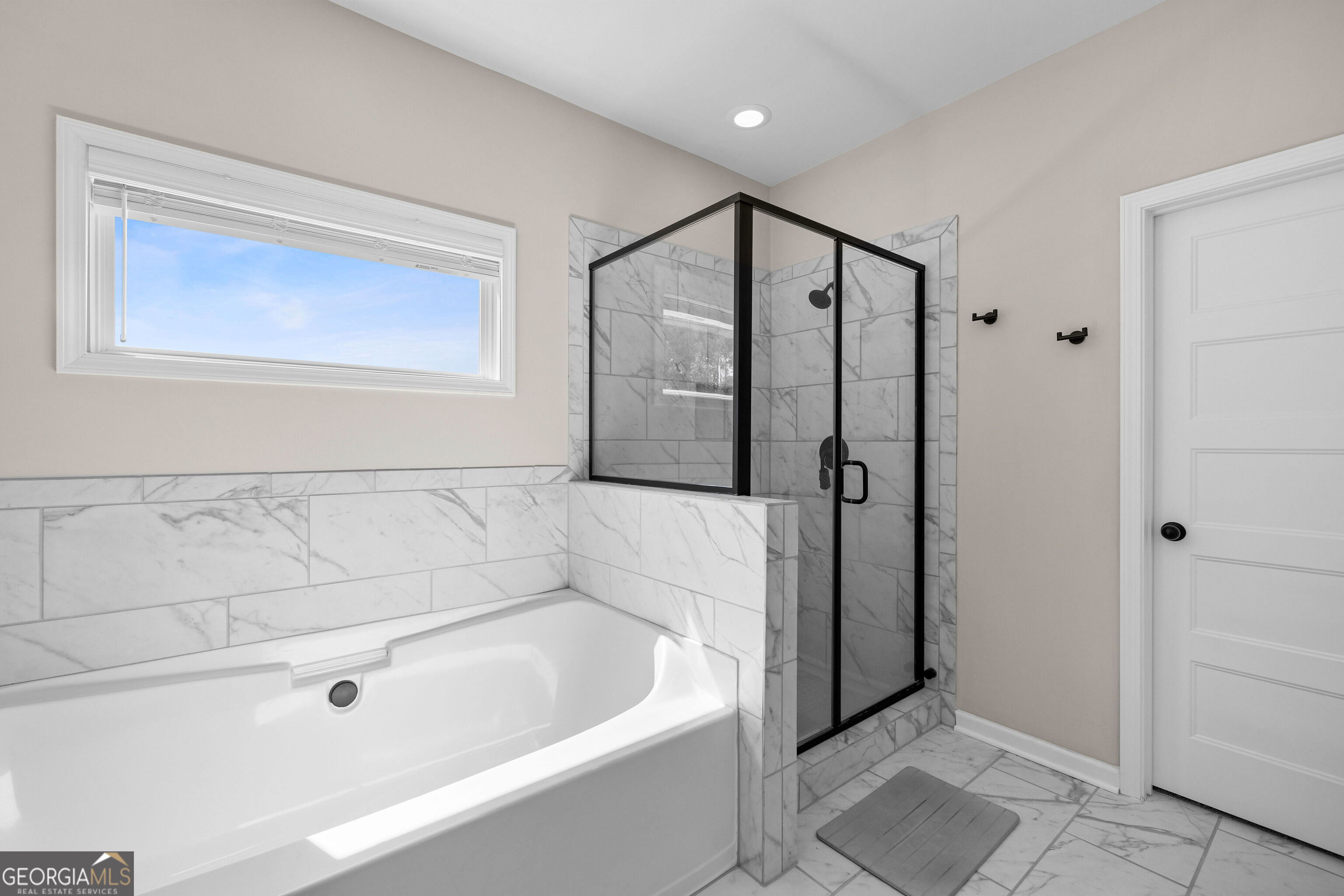 Bathroom with a marble-tiled soaking tub and glass-enclosed shower with black framing.