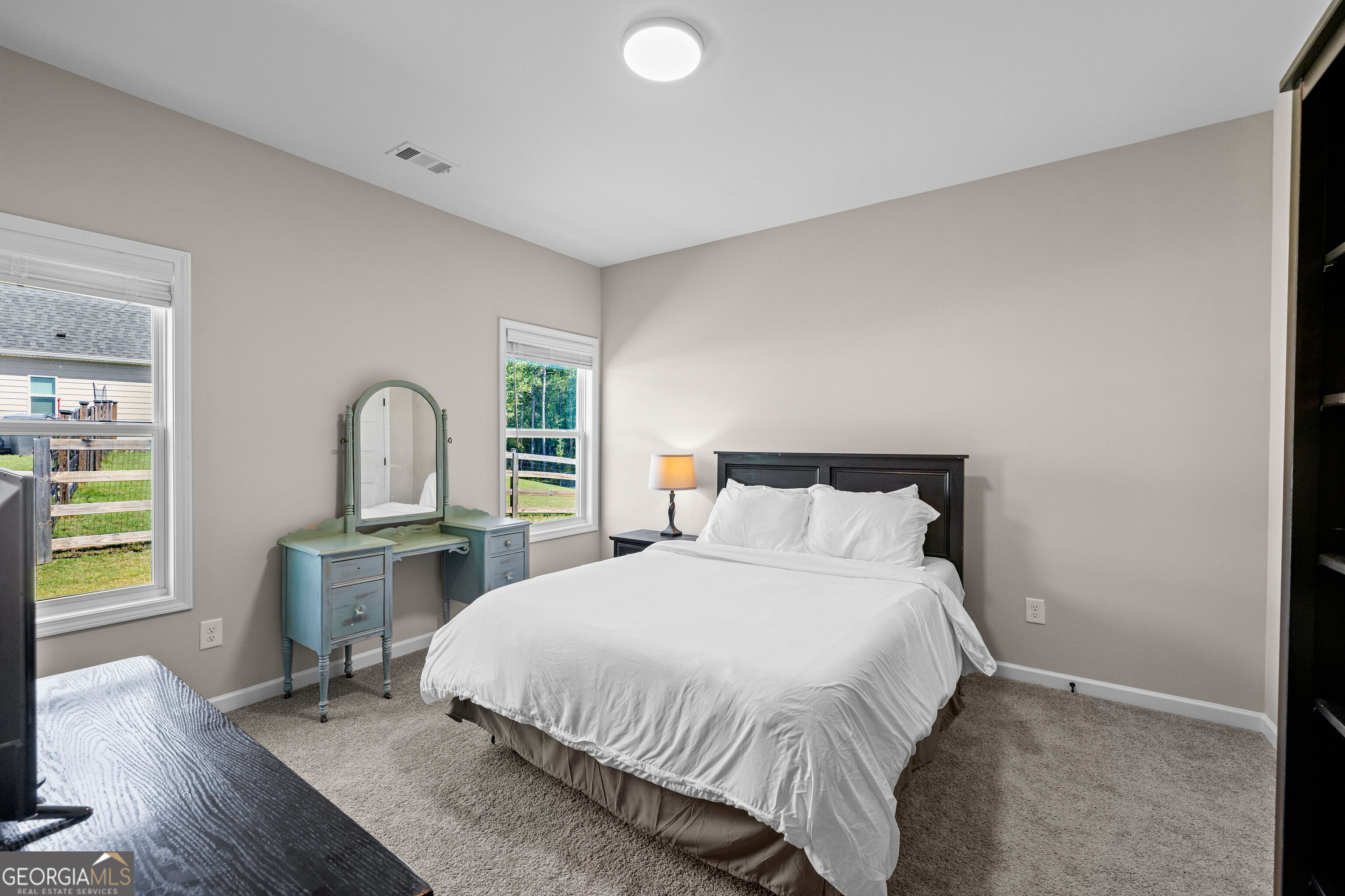 Bedroom with a large white bed and blue-green vanity between two windows.