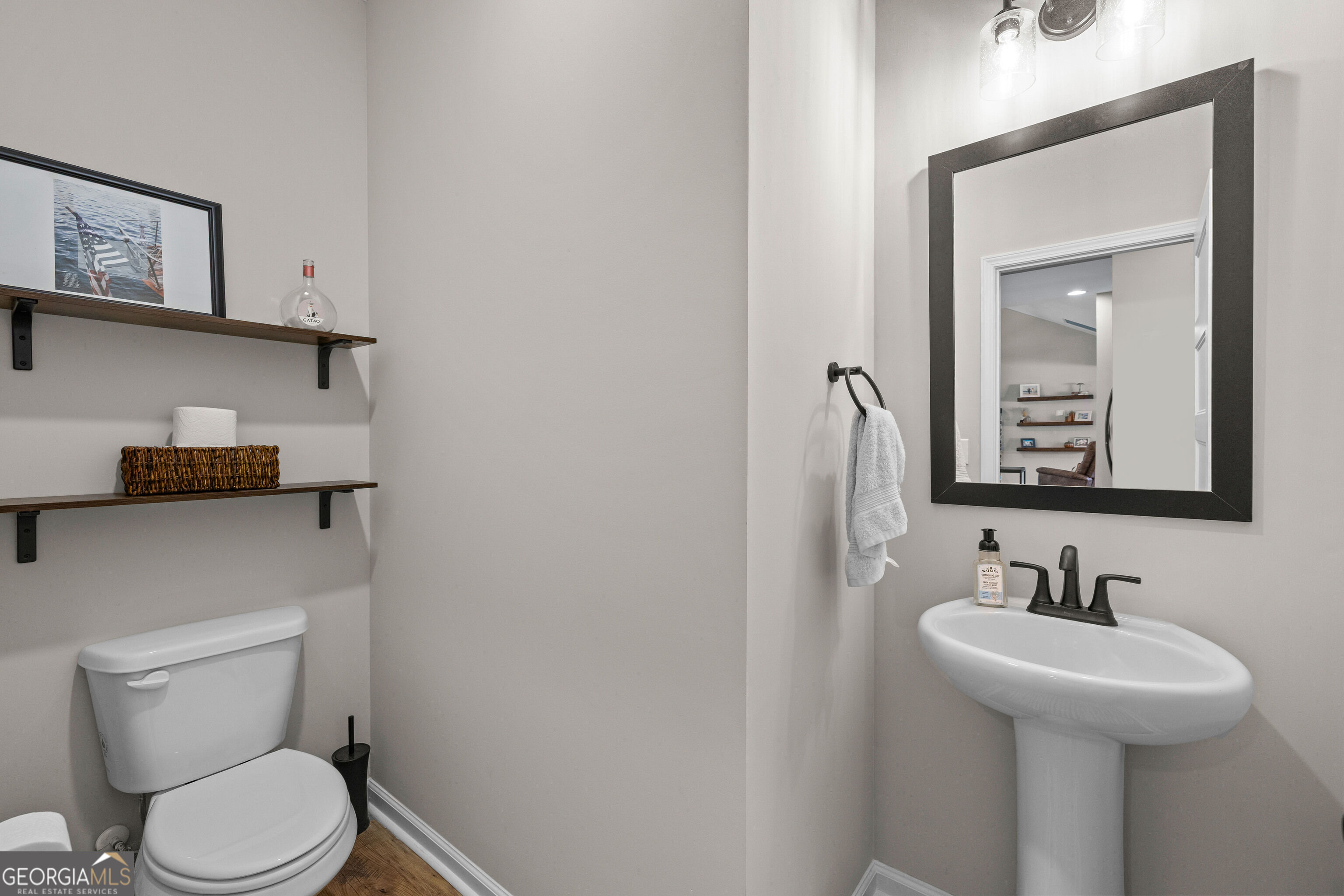 Bathroom with a white toilet, pedestal sink, black-framed mirror, and dark wood shelves.