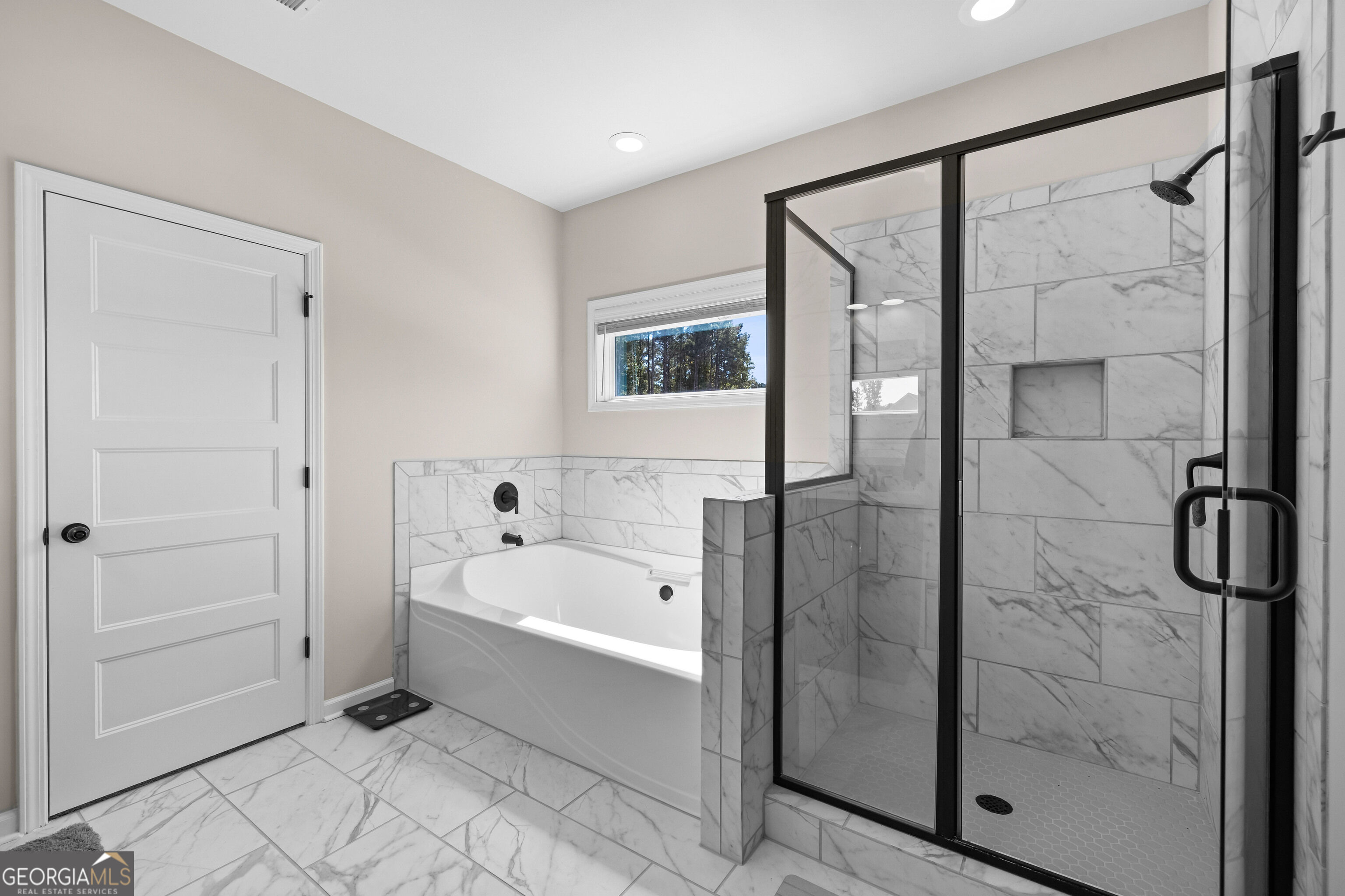 Bathroom with a white soaking tub, marble-look tile, and a black-framed glass shower.