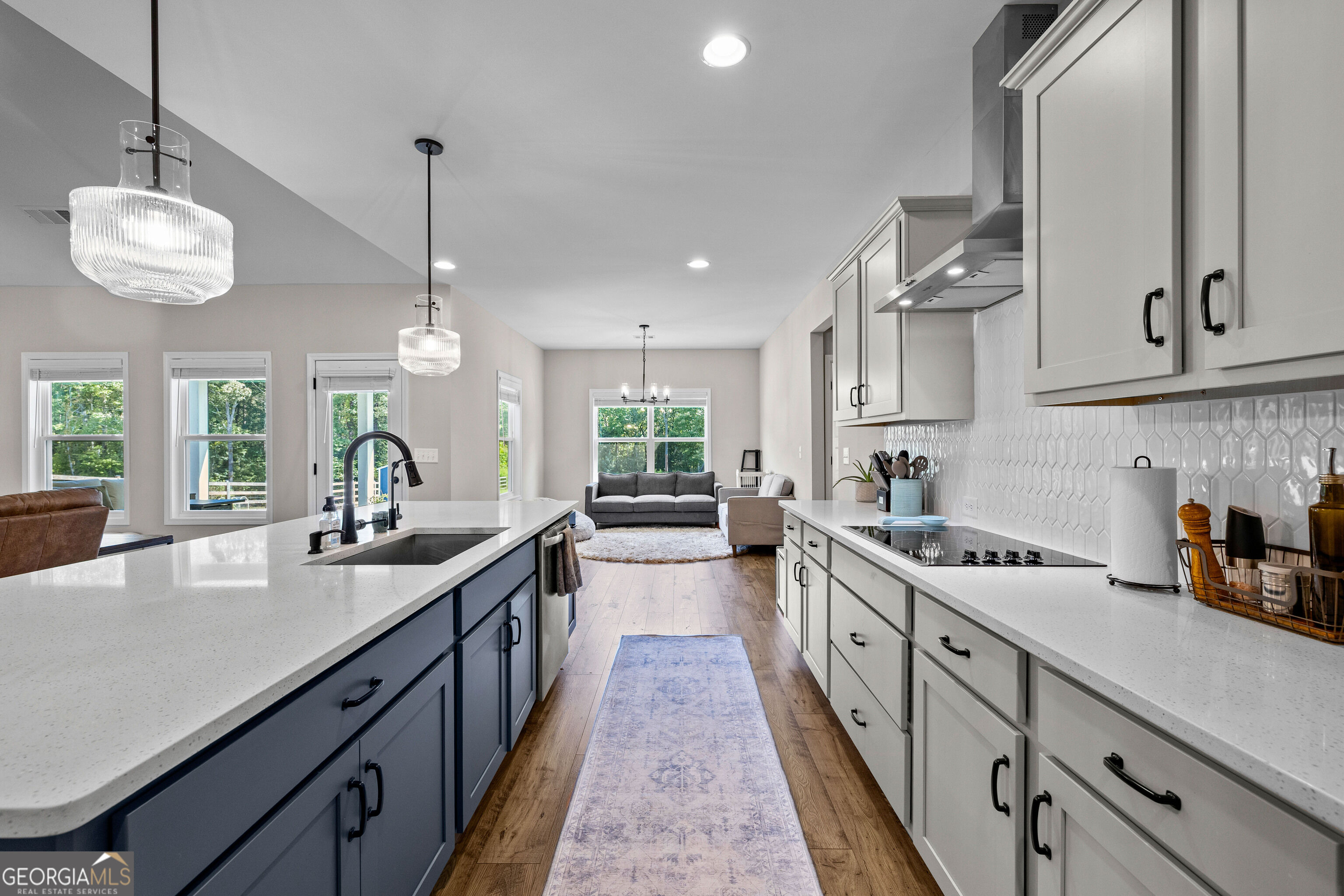 Kitchen with a large quartz island and dark blue cabinets, opening into a furnished living area.