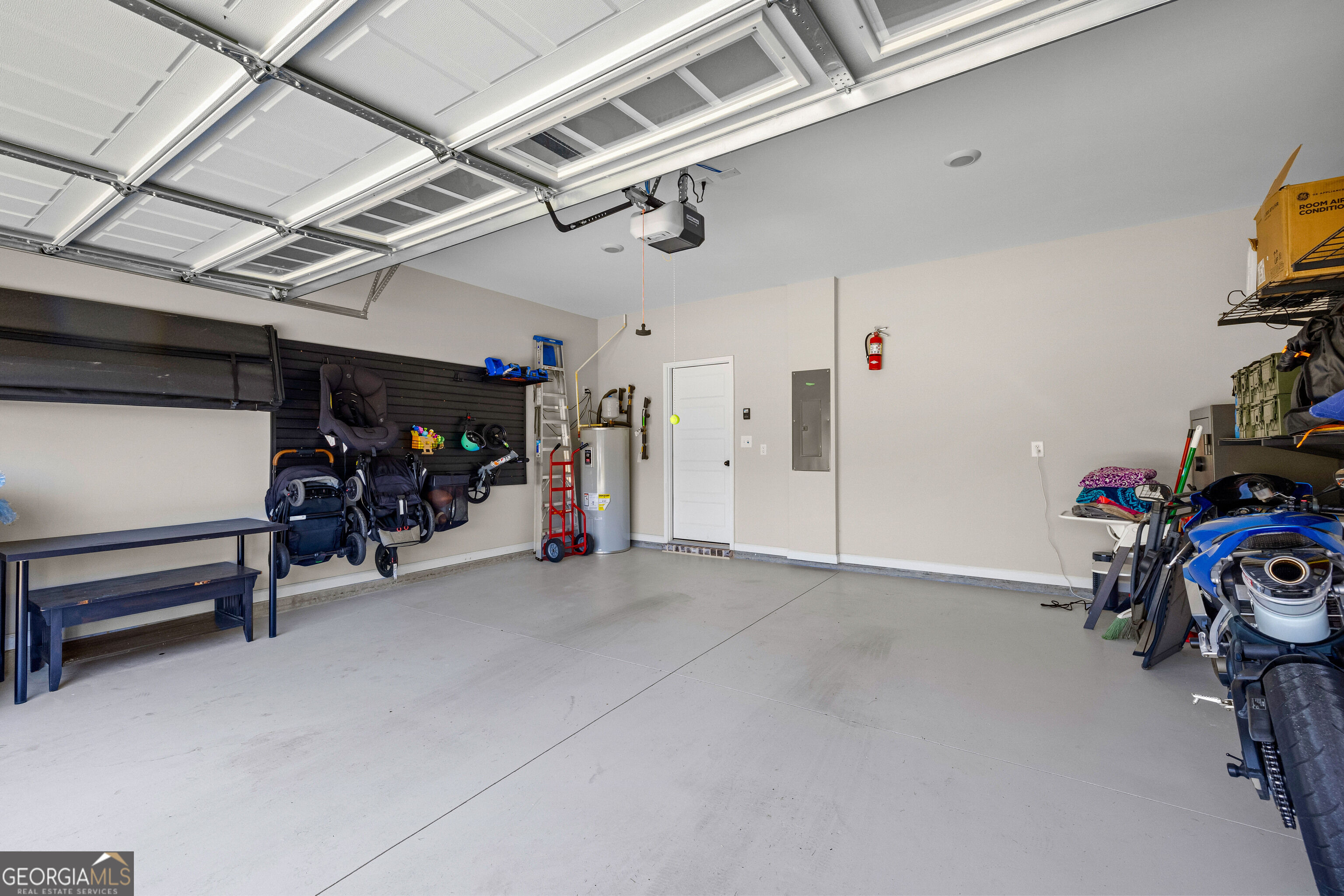 Garage with a raised overhead door, concrete floor, wall storage, and recreational equipment.