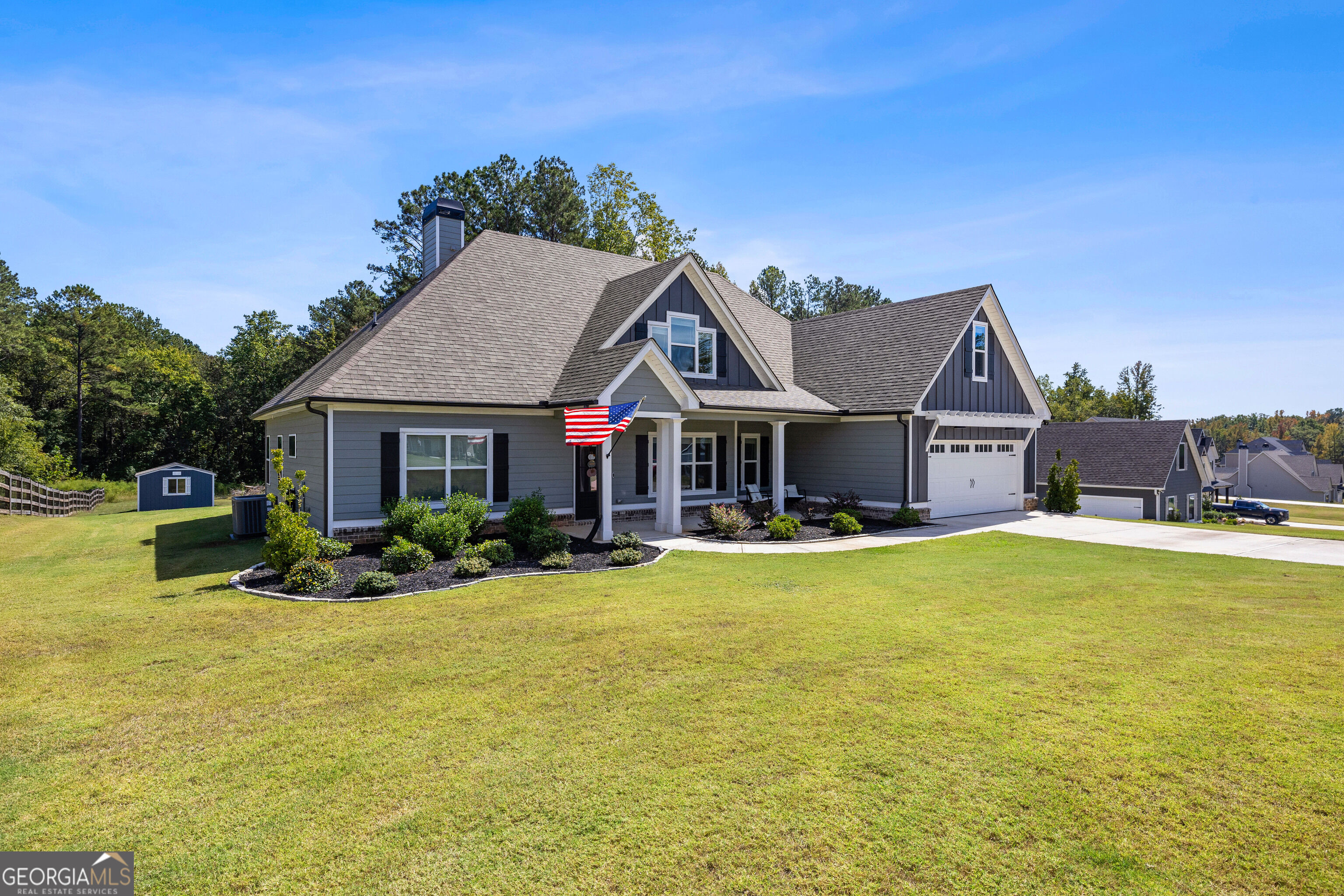 Gray house with covered porch, attached garage, American flag, and broad front lawn.
