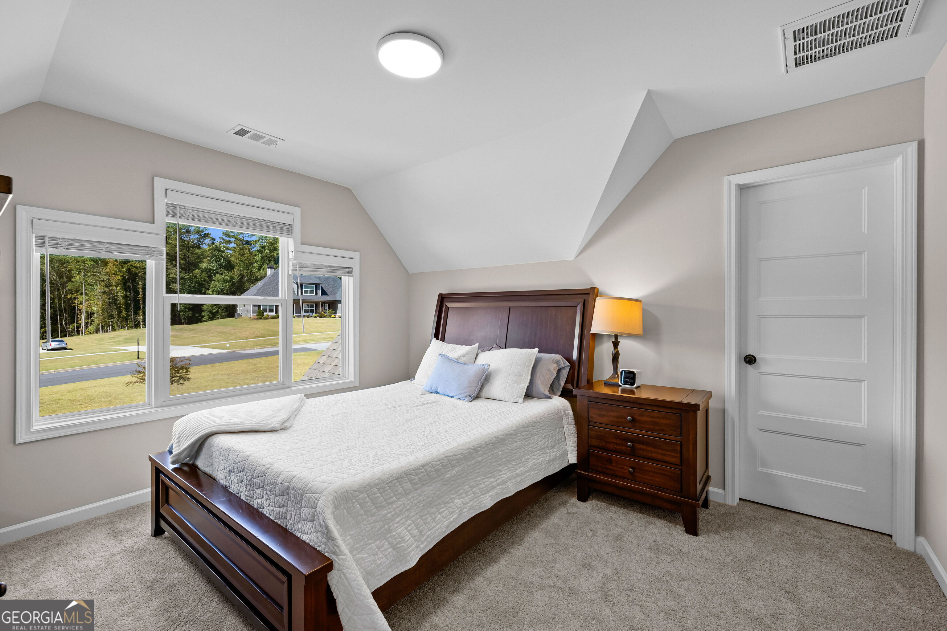 Furnished bedroom with a dark wood bed and large windows overlooking a lawn and trees.