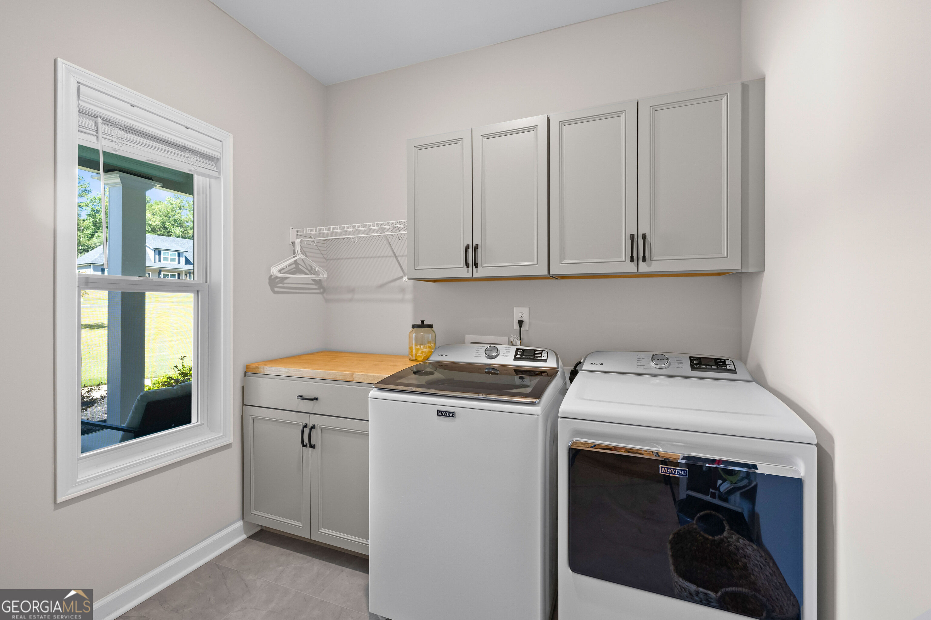 Laundry room with gray cabinets, washer and dryer, and a window overlooking the yard.