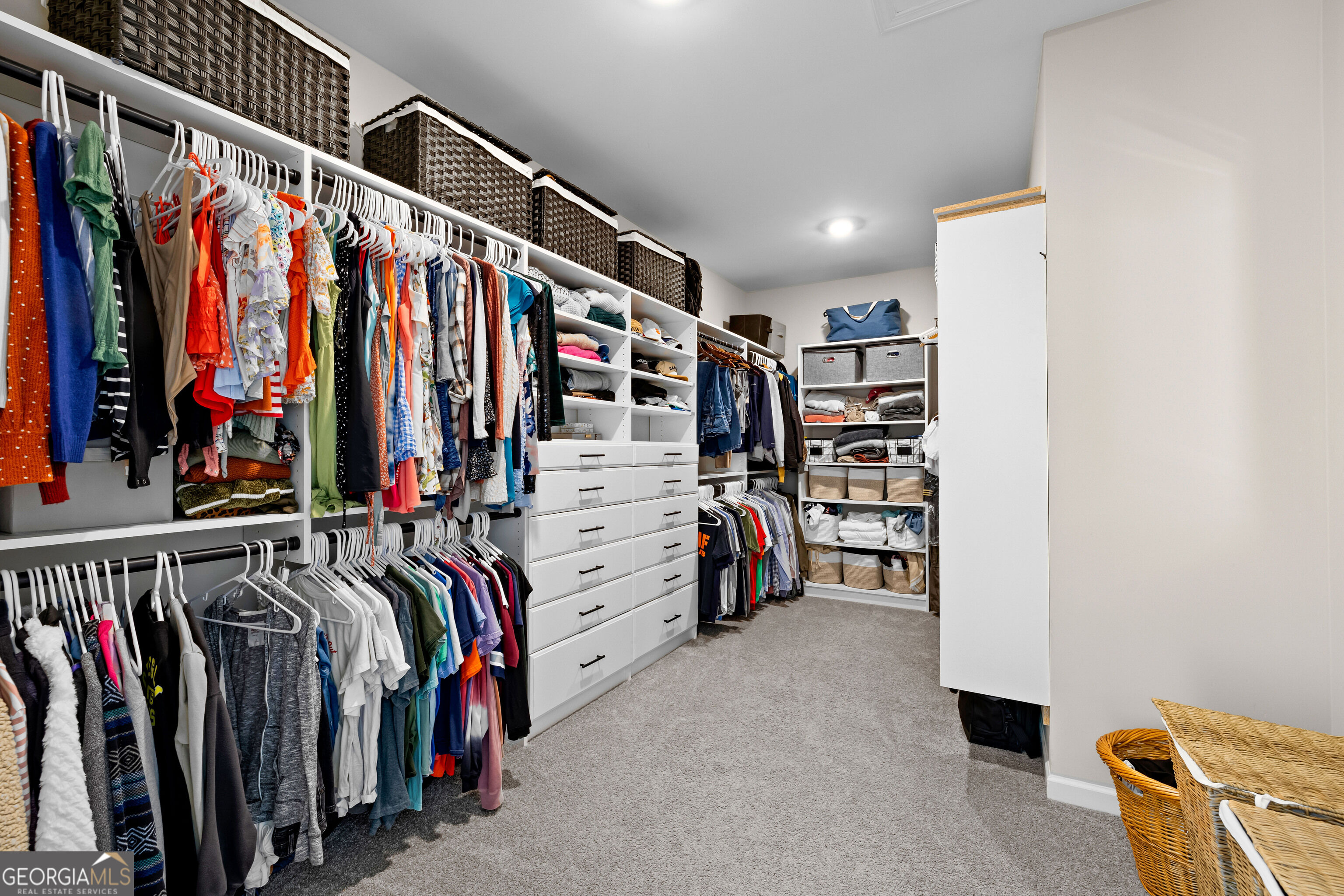 Walk-in closet with white built-in drawers, extensive clothing storage, and woven baskets.