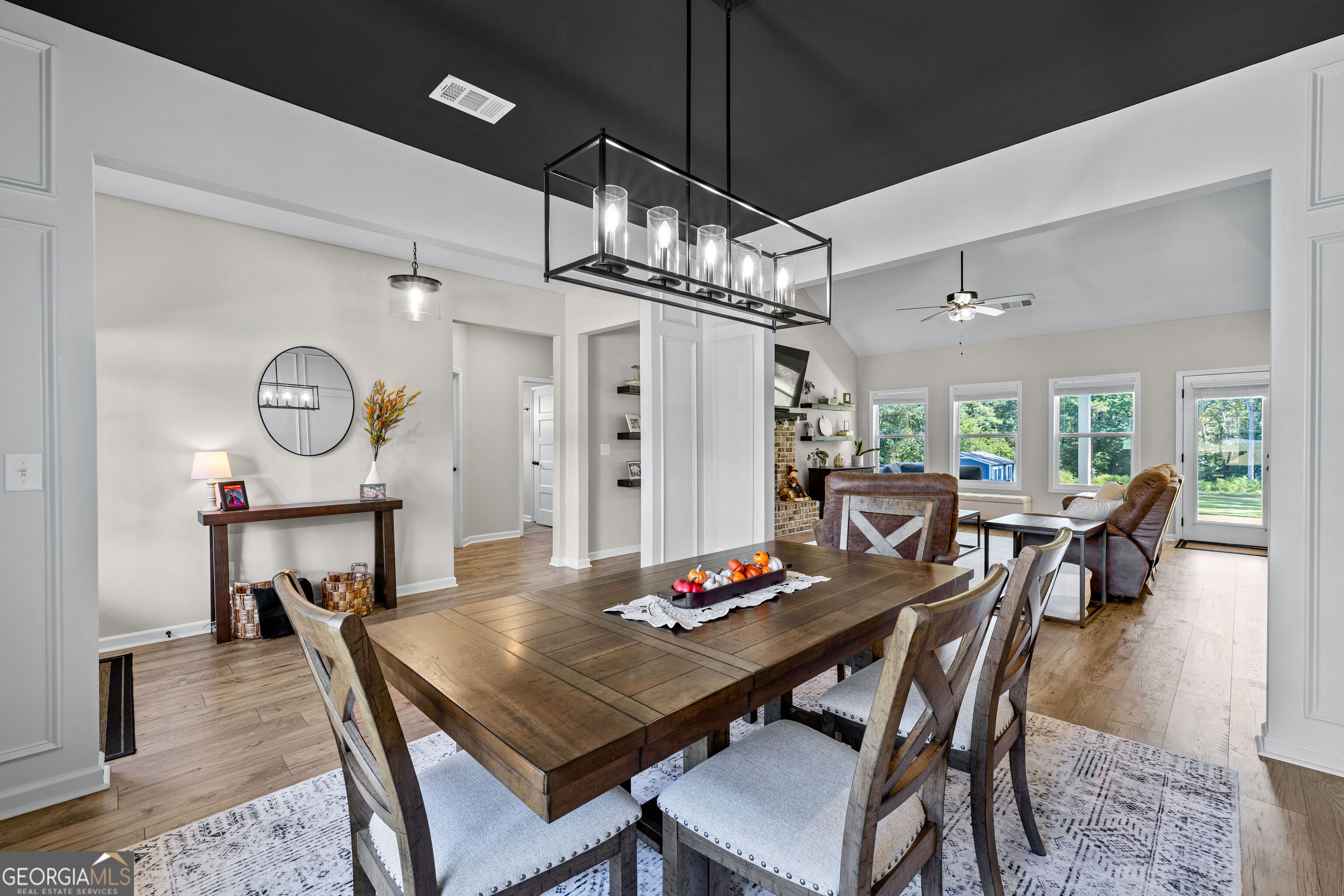 Dining room with a large wood table and chandelier opening into a bright living area.