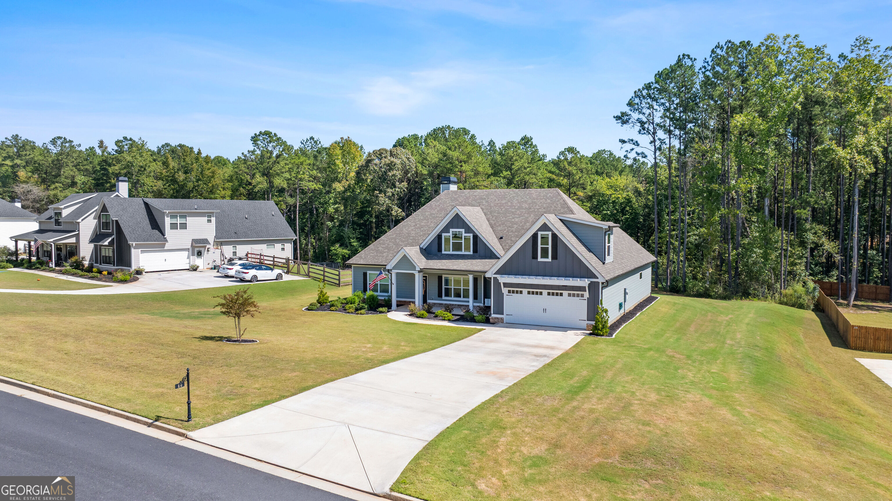 Gray-blue two-story home with a front garage, broad driveway, and wooded backdrop.