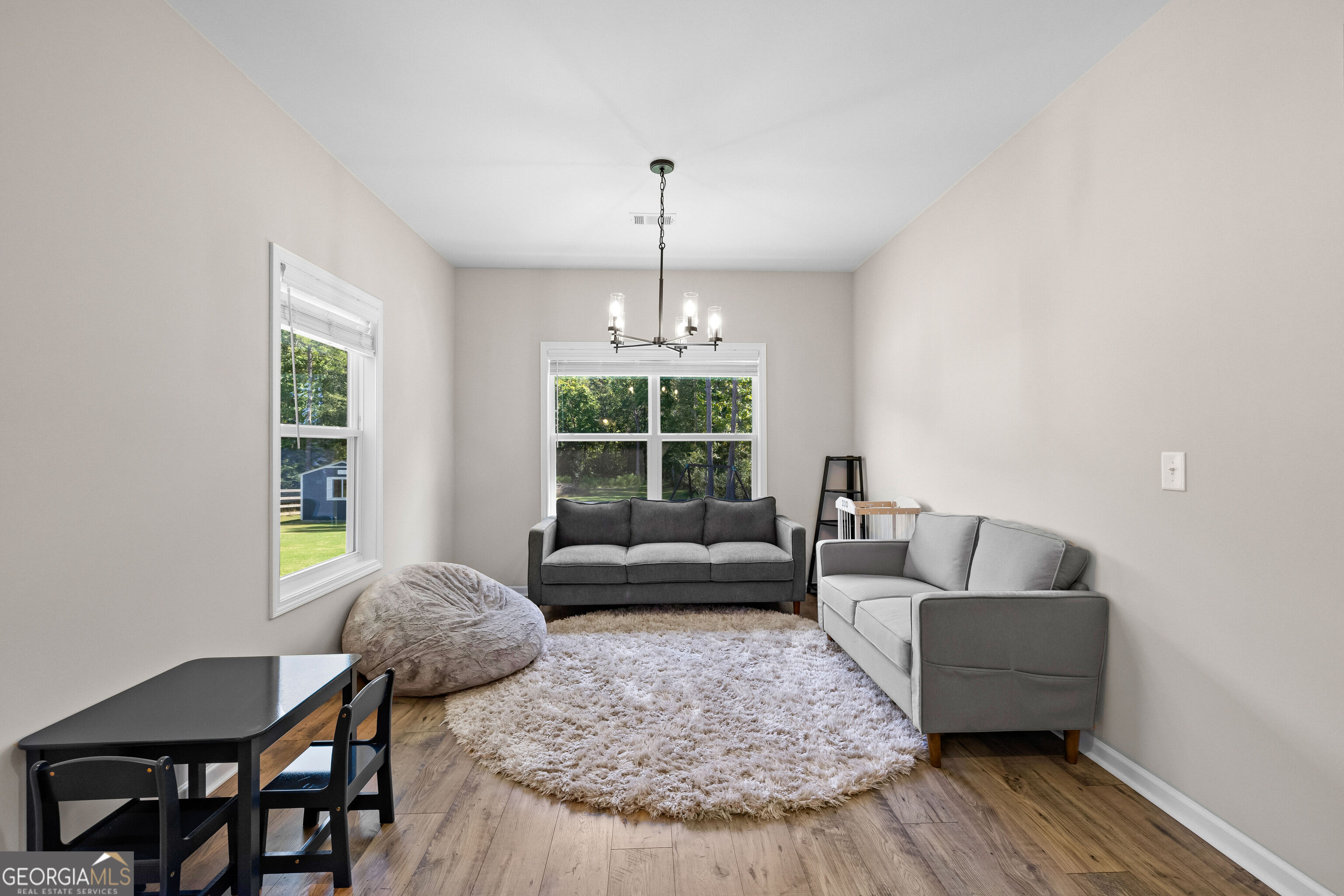 Staged living room with gray sofas, a shag rug, and windows overlooking a green yard.