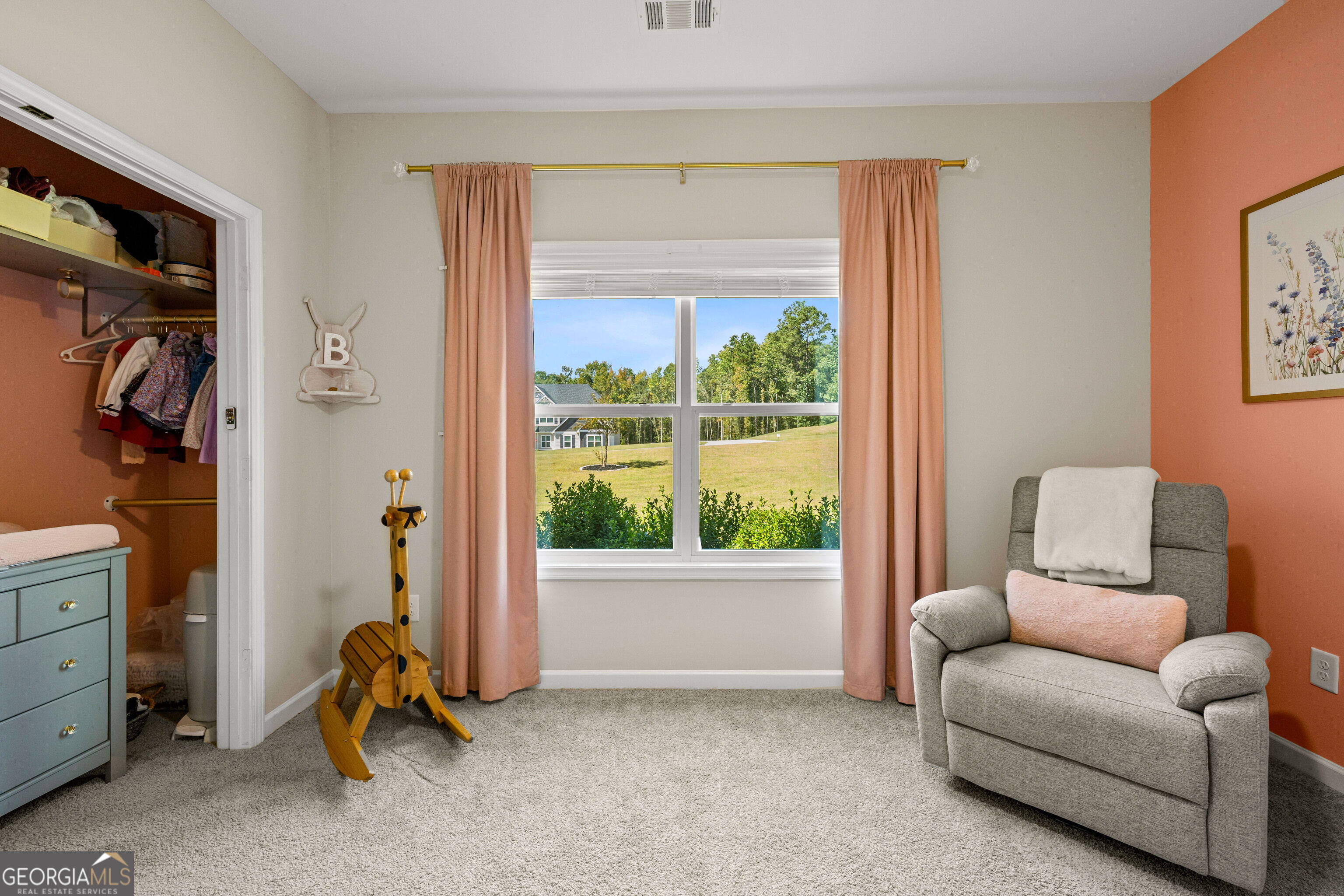 Furnished bedroom with peach curtains, a toy rocking horse, and a window overlooking a green lawn.