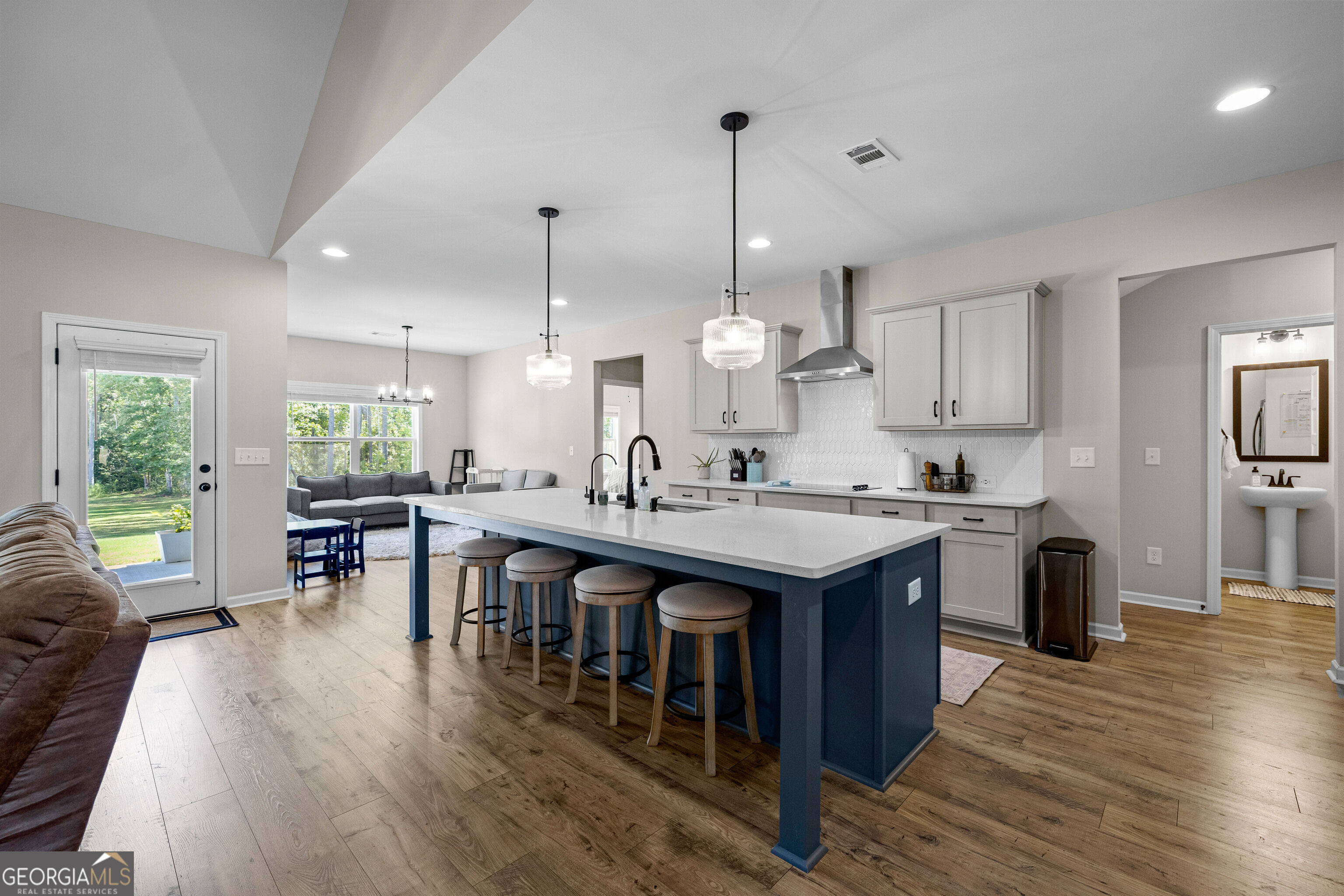 Open-plan kitchen with a large navy island, four stools, white cabinetry, and a hexagonal tile backsplash.