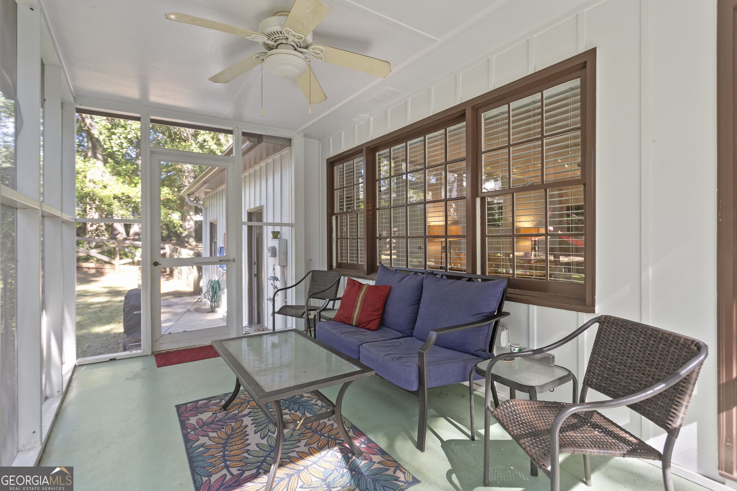 Screened porch with a blue sofa, wicker chairs, glass-top table, and brown-trimmed windows.
