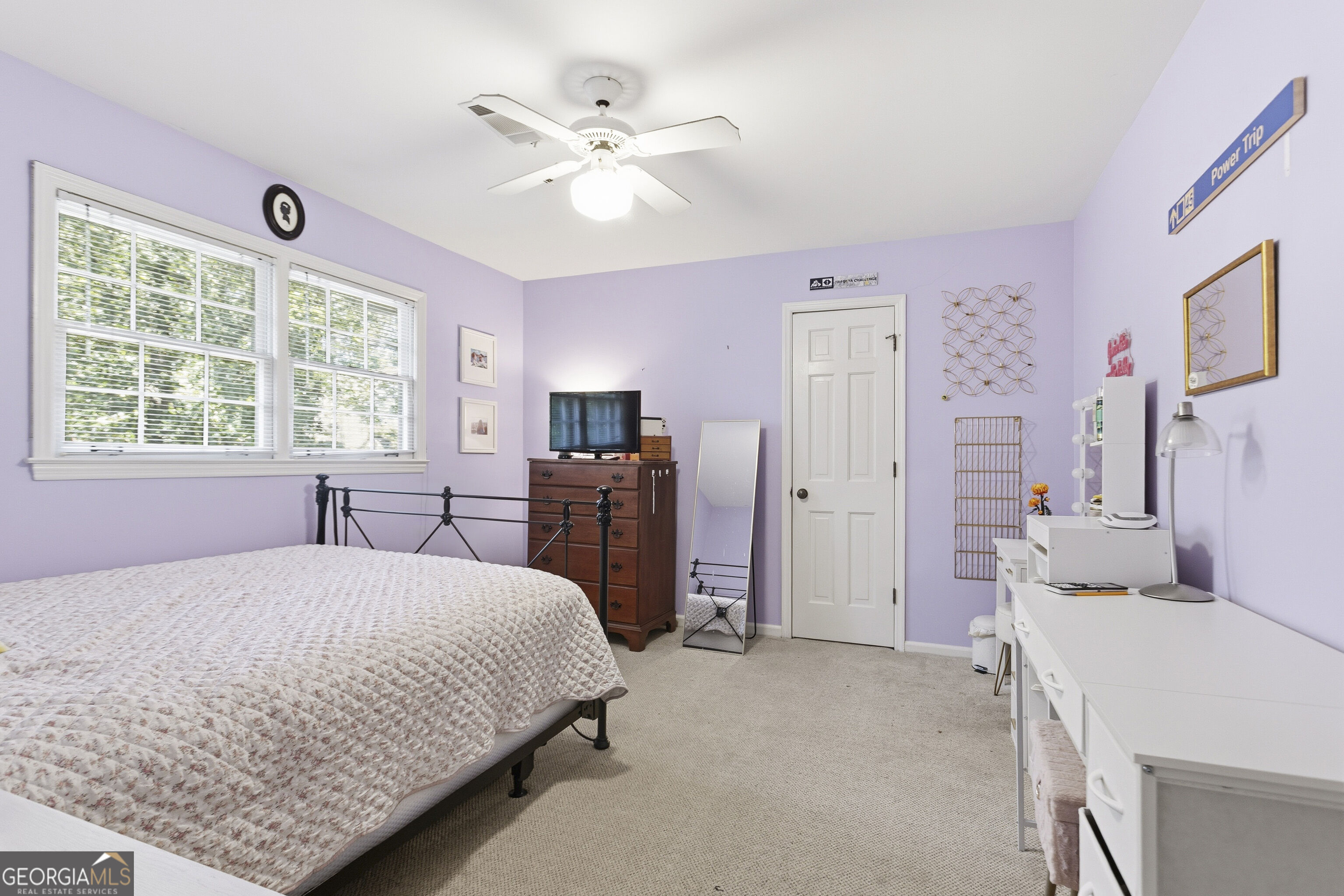 Bedroom with lavender walls, a black metal bed, large windows, and a white vanity.