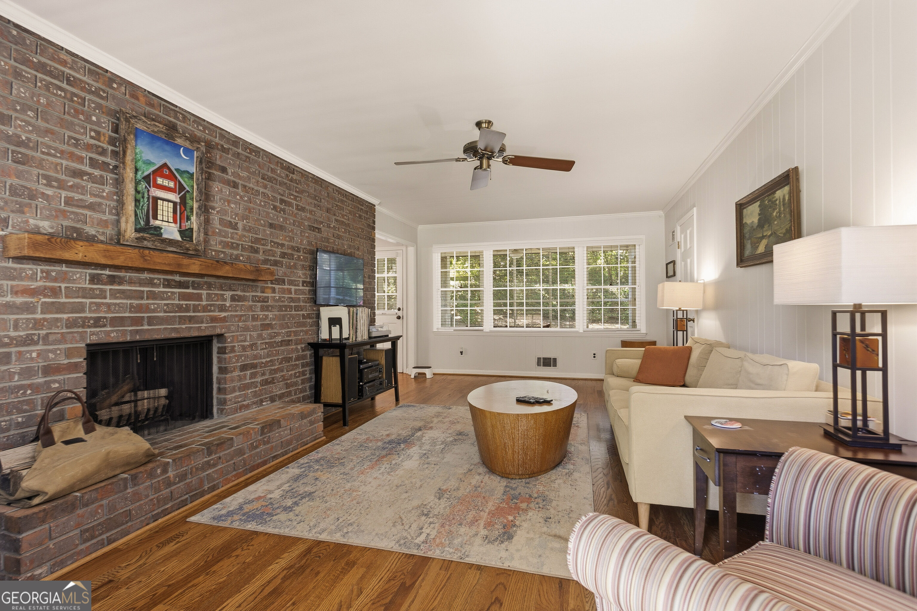 Living room with a brick fireplace, cream sectional, hardwood floors, and wide windows.