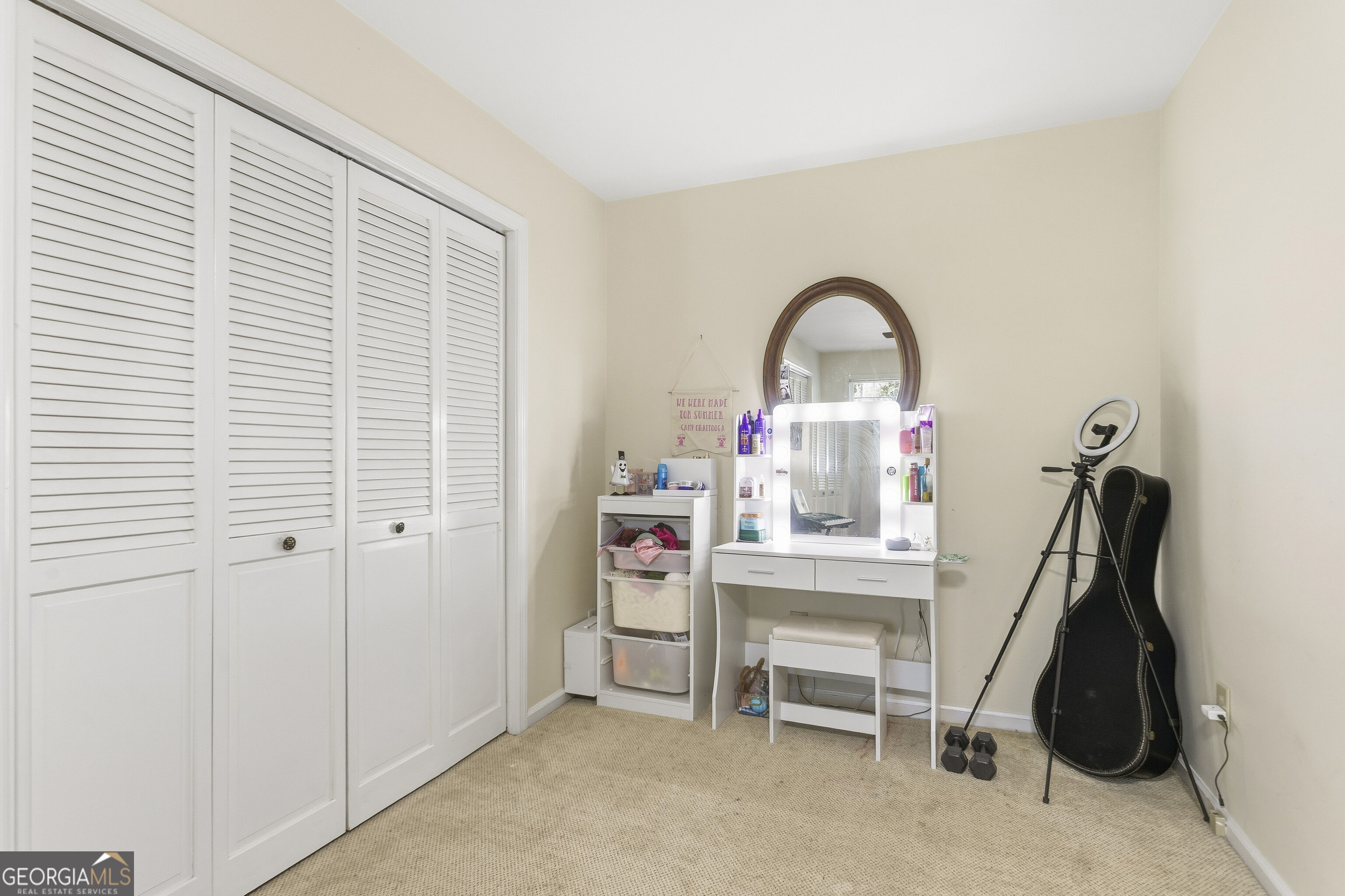 Bedroom dressing area with louvered closet doors, illuminated vanity mirror, ring light, and guitar case.