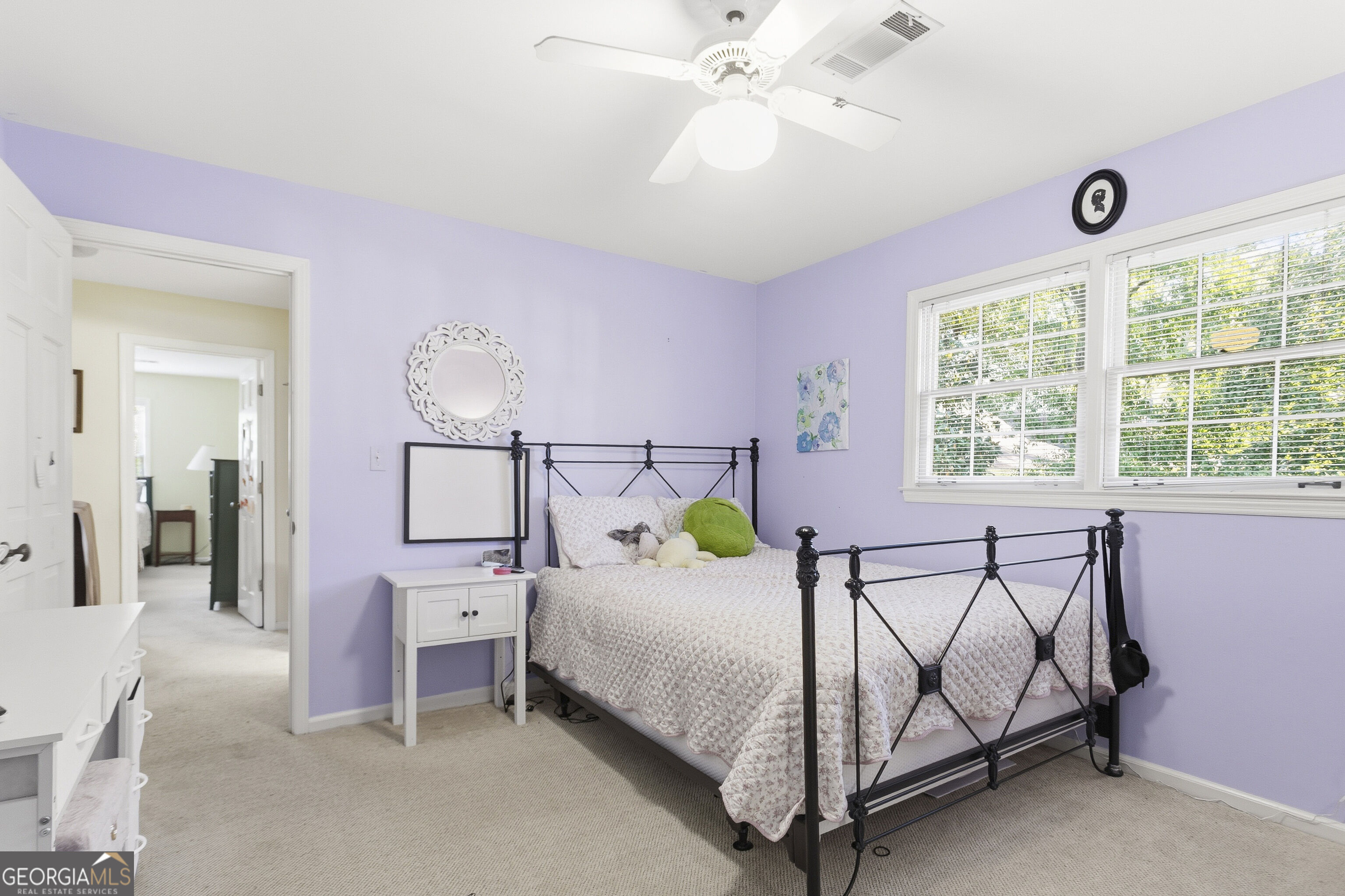 Bedroom with lavender walls, a black metal bed, and two large windows with white blinds.