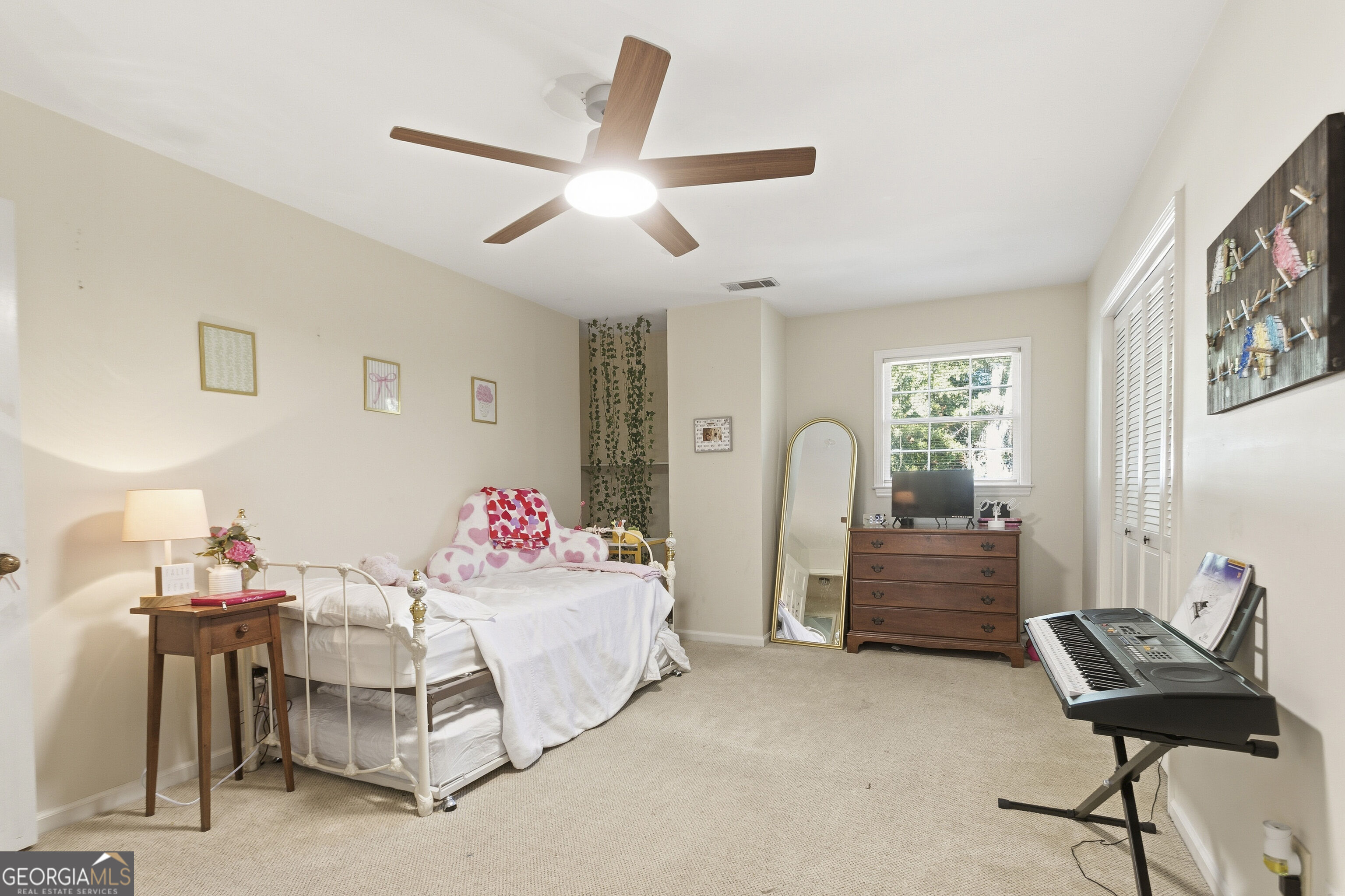 Furnished bedroom with a white metal bed, heart-patterned bedding, and an electronic keyboard.