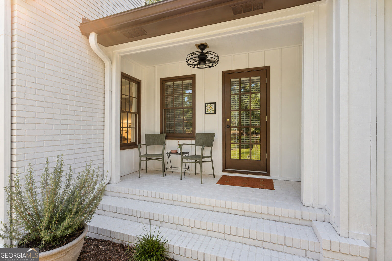 Front porch with white brick steps, a brown glass-paneled door, and two chairs beside a small table.