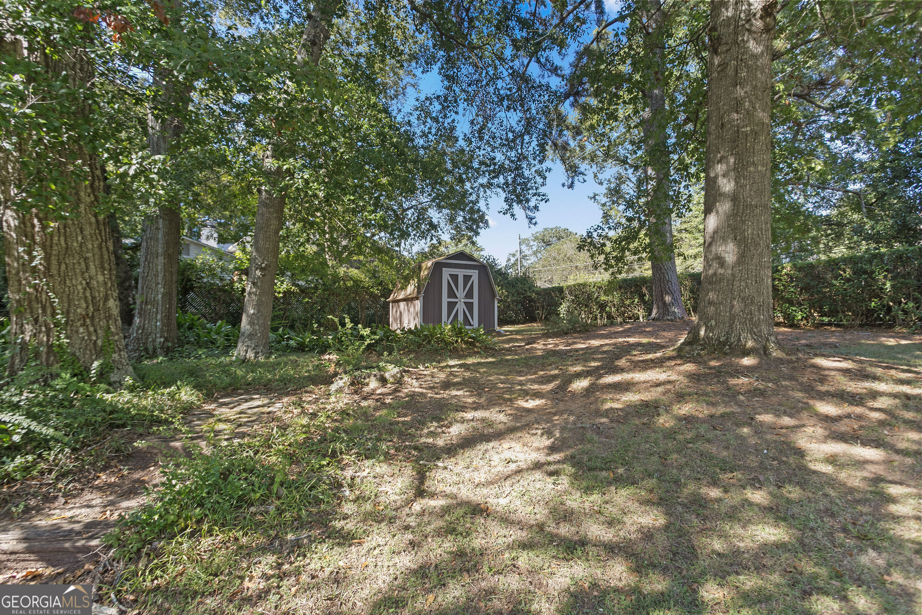 Shaded backyard with a brown storage shed, mature trees, and a patchy lawn.