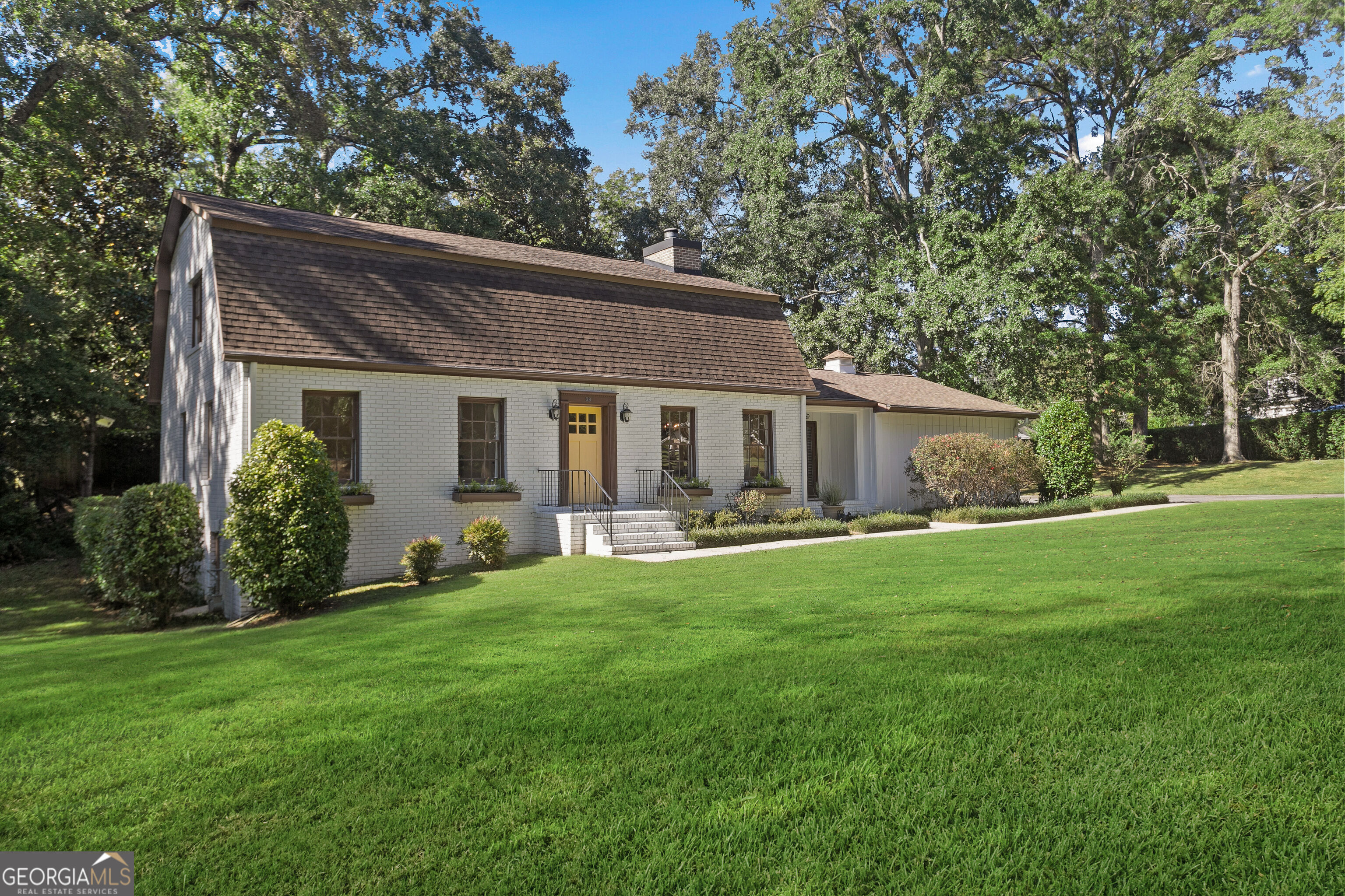 White brick home with yellow front door, broad lawn, and mature trees.