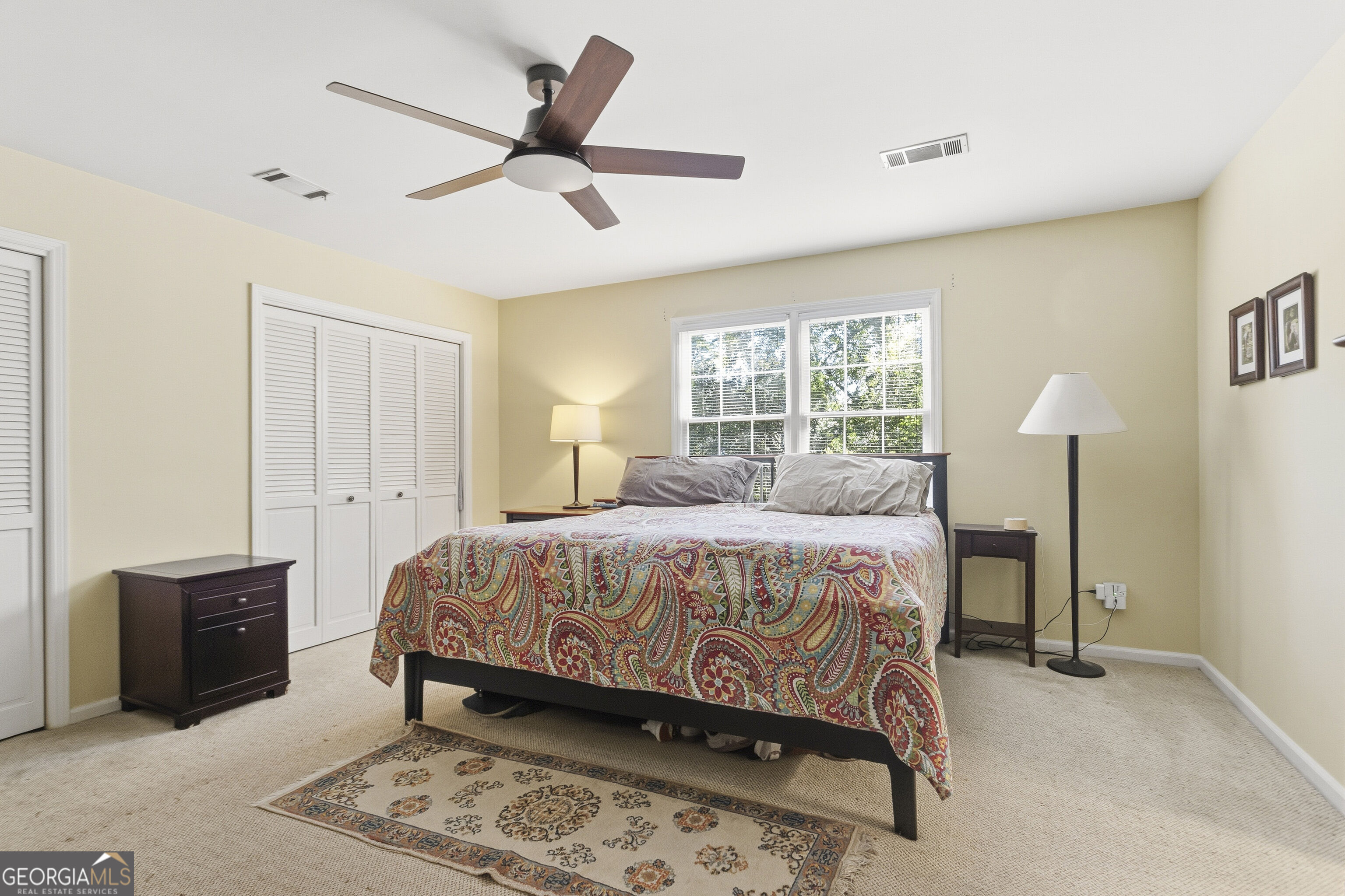 Bedroom with a colorful paisley bedspread, white closet doors, and a ceiling fan.