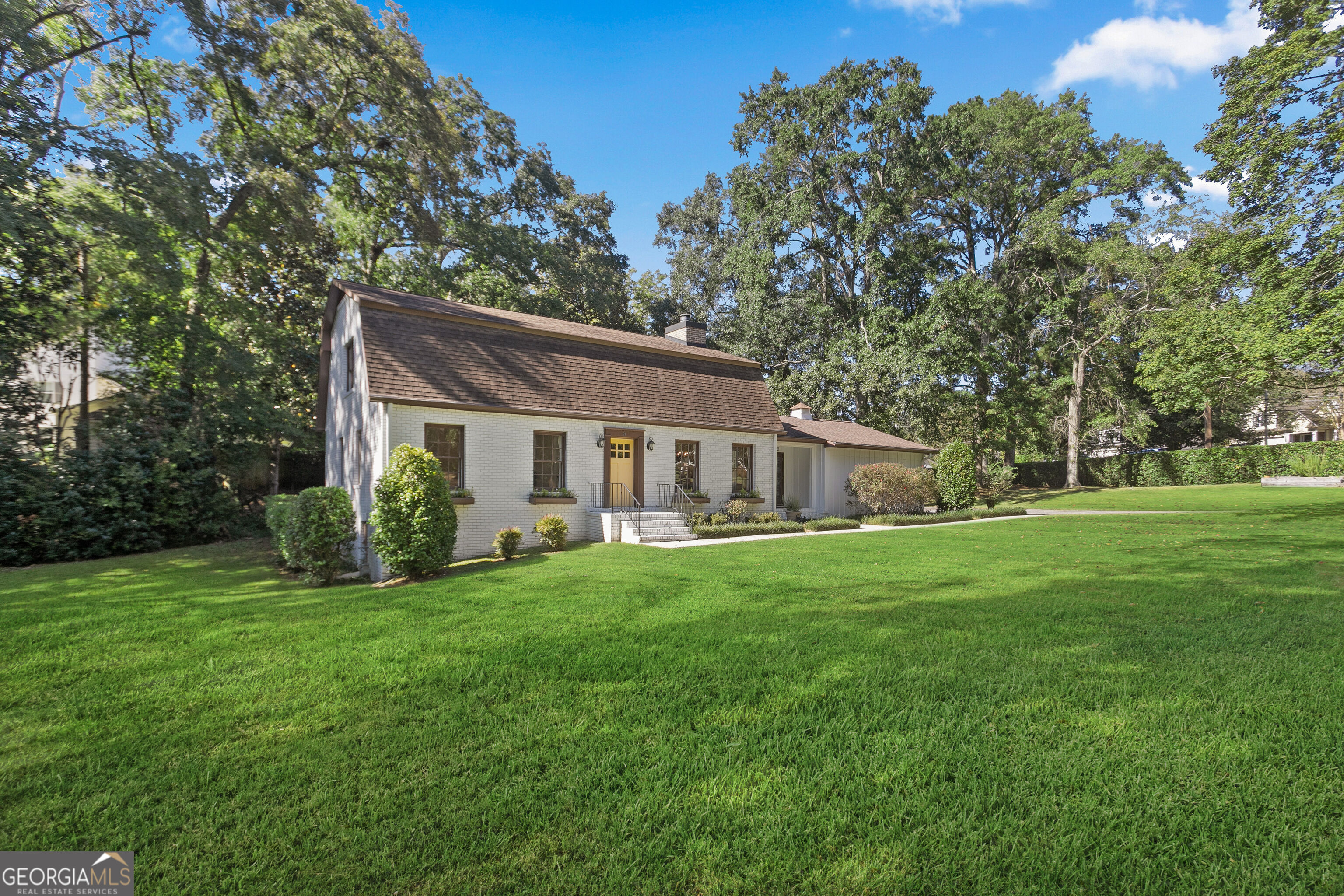 White-brick house with a steep brown roof and yellow front door beyond a broad lawn.