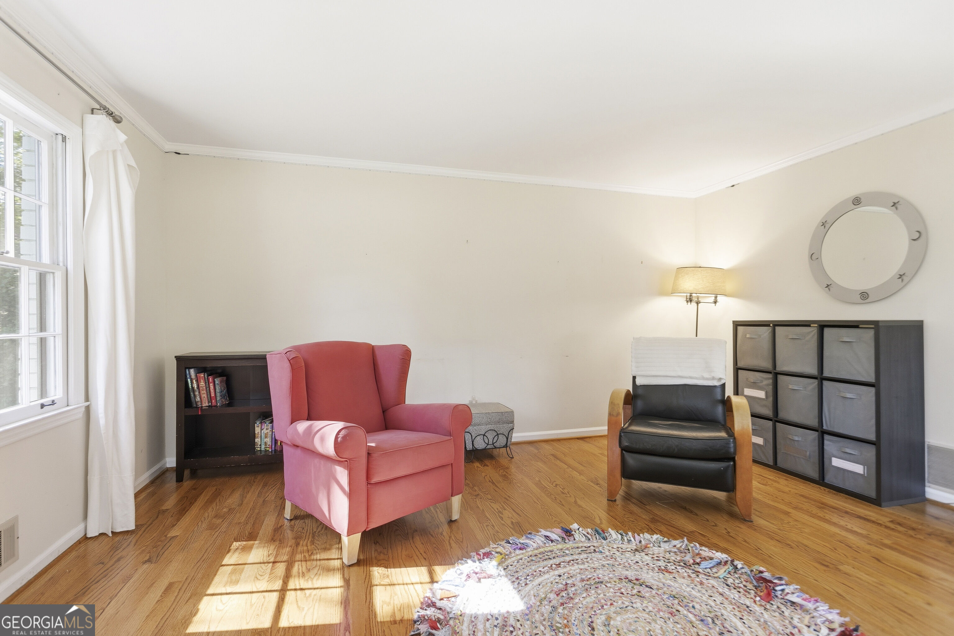 Sitting room with pink and black armchairs, hardwood floors, and a colorful braided rug.