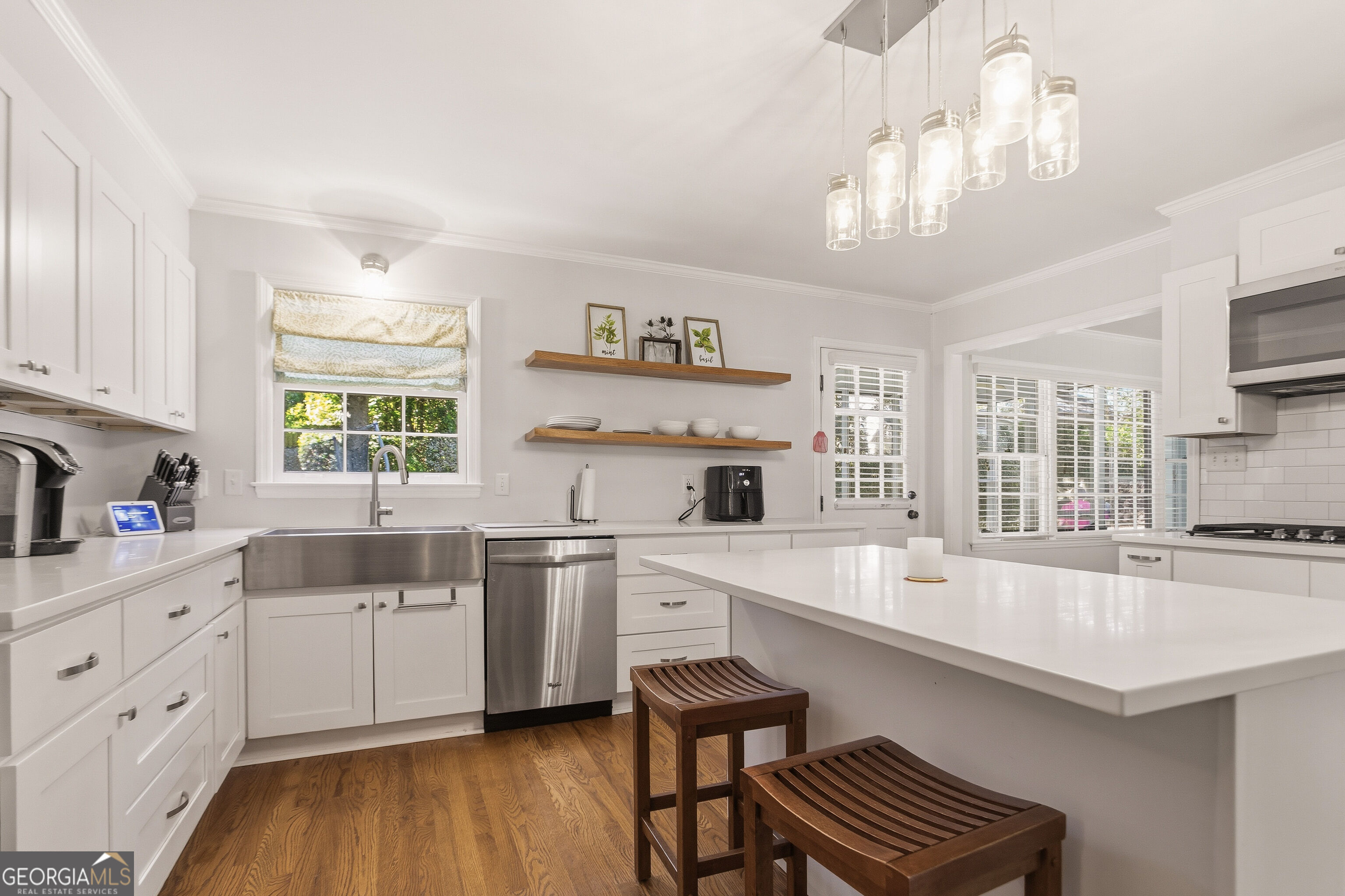 Bright white kitchen with a large island, stainless steel appliances, and glass pendant lights.