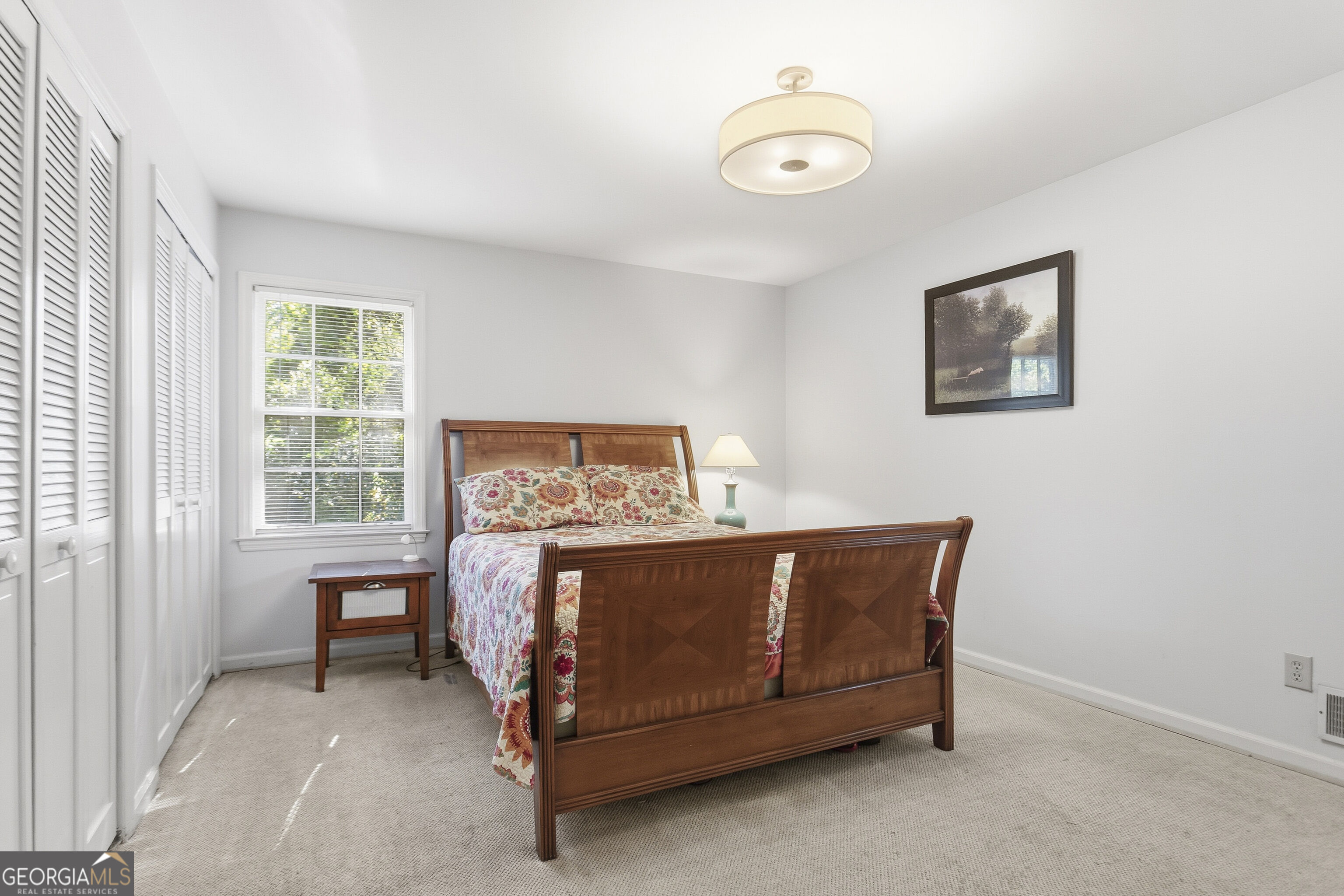 Bedroom with a wooden bed, floral bedding, louvered closets, and a bright window.