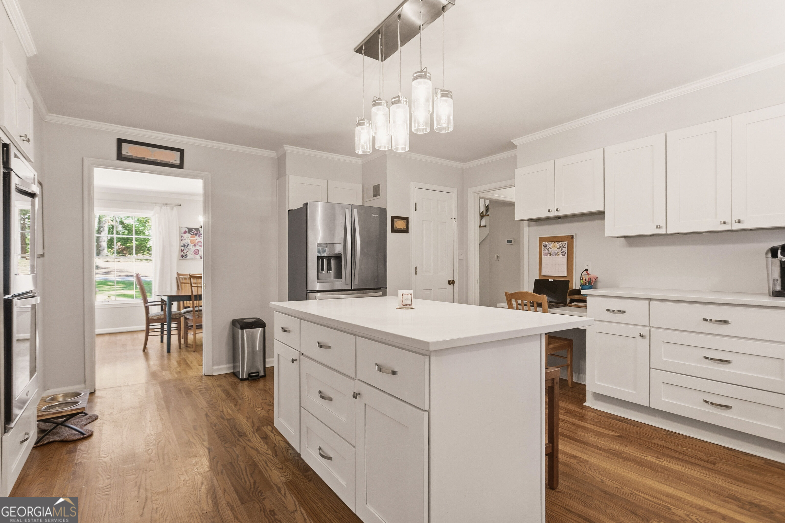 Kitchen with a large white island, stainless steel appliances, and hardwood floors.