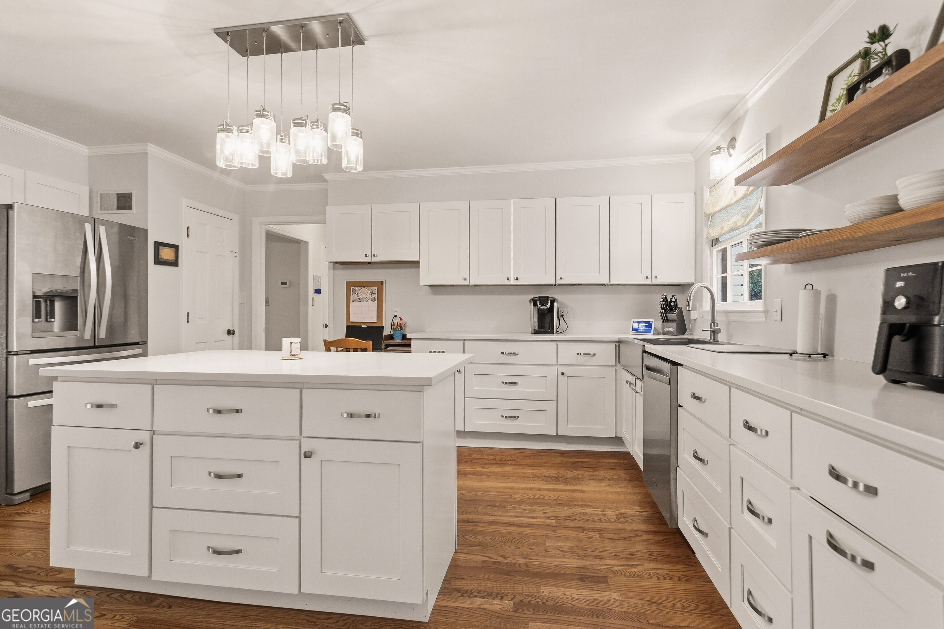 Bright white kitchen with a large island, stainless steel appliances, and warm wood floors.